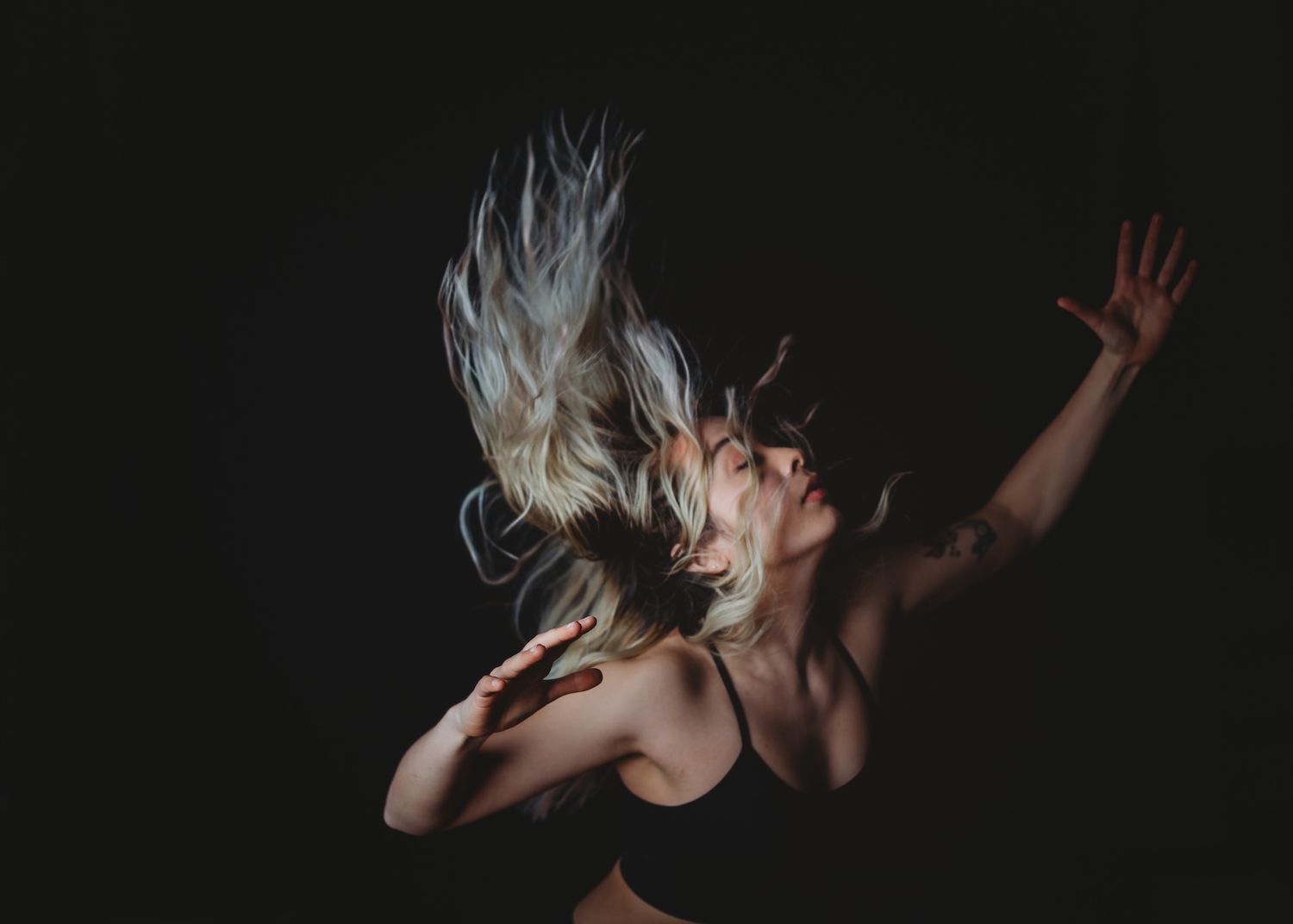 Dramatic dancer photographed against dark background with hair flying and arm raised in expressive motion.