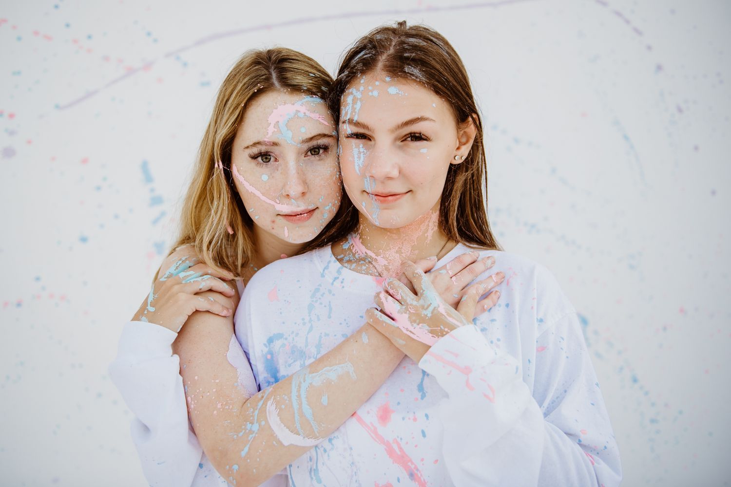Two people in white outfits embracing while posing against white background.