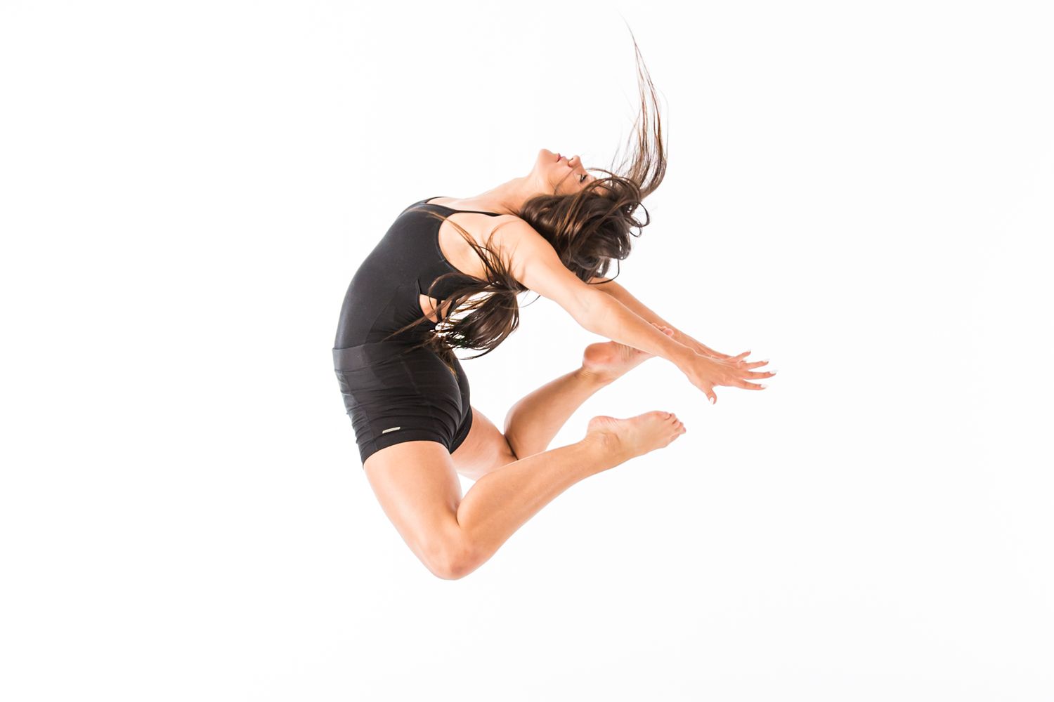 Athletic dancer performs midair jump in black leotard against white background.