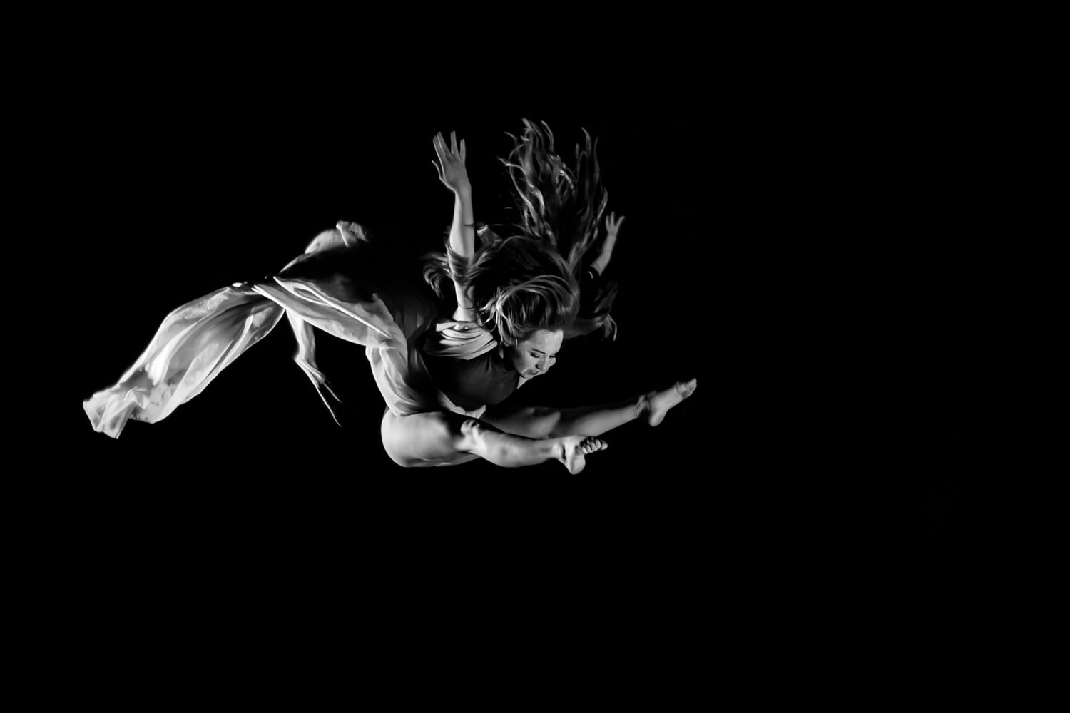 Expressive dance movement captured in black and white with flowing fabric against dark background.