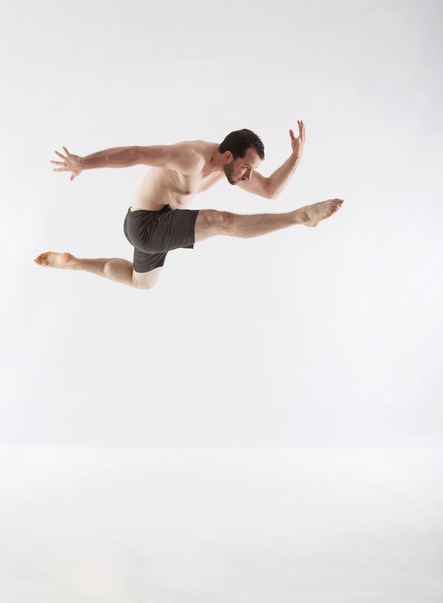 A male dancer executes a dramatic mid-air split leap against a white background.