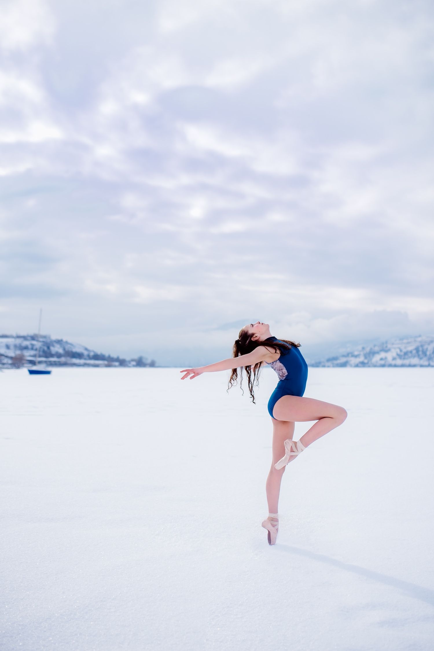 Ballet dancer performs graceful pose en pointe on snowy landscape with mountains in background.