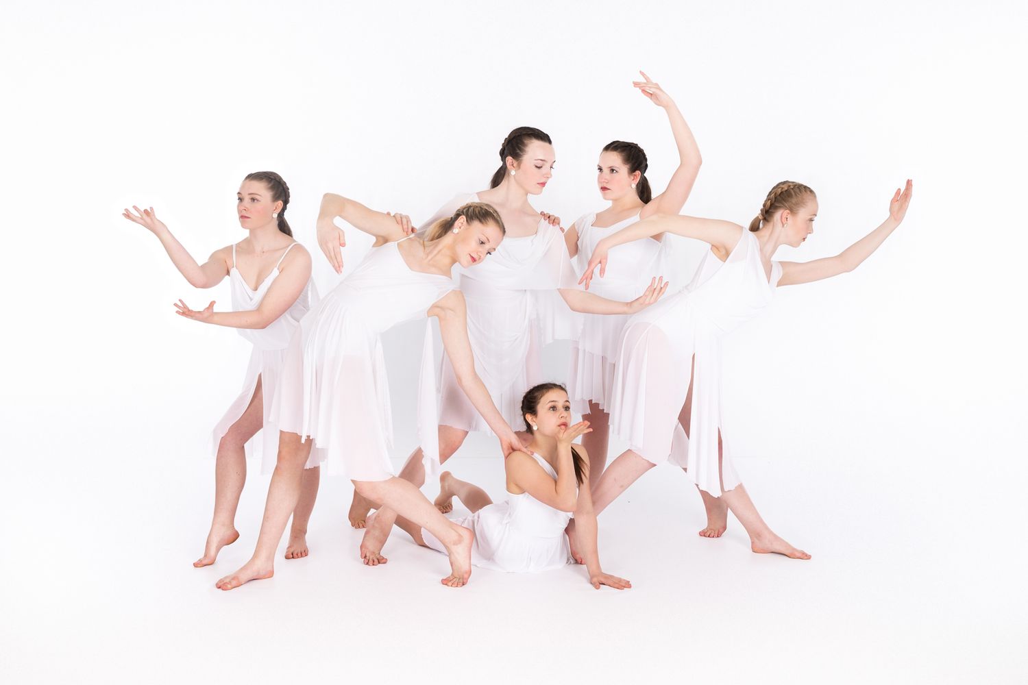 Dance performers in flowing white dresses strike graceful poses against a white backdrop in contemporary style.