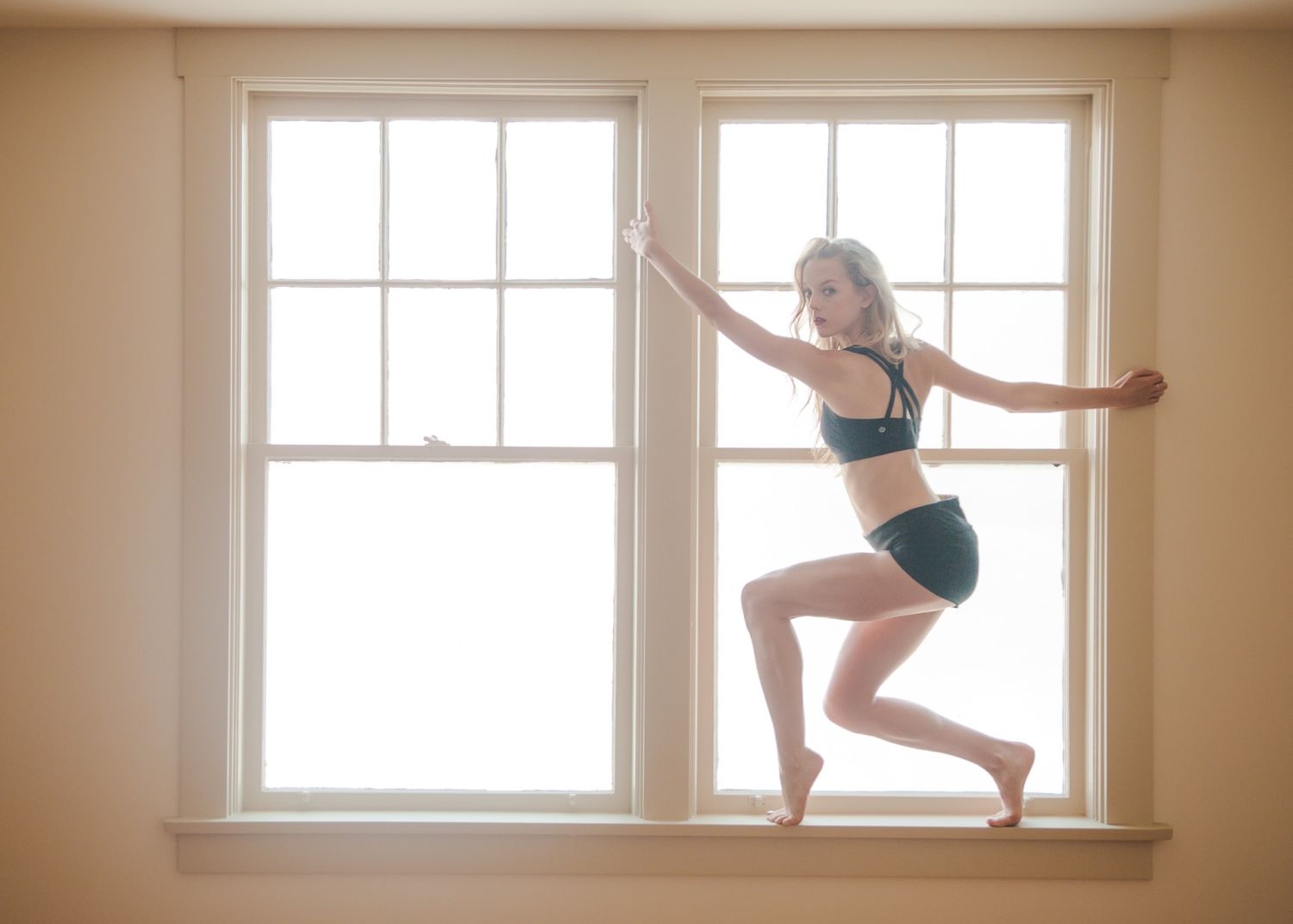 Graceful dance movement captured in silhouette against bright window light in minimal interior setting.