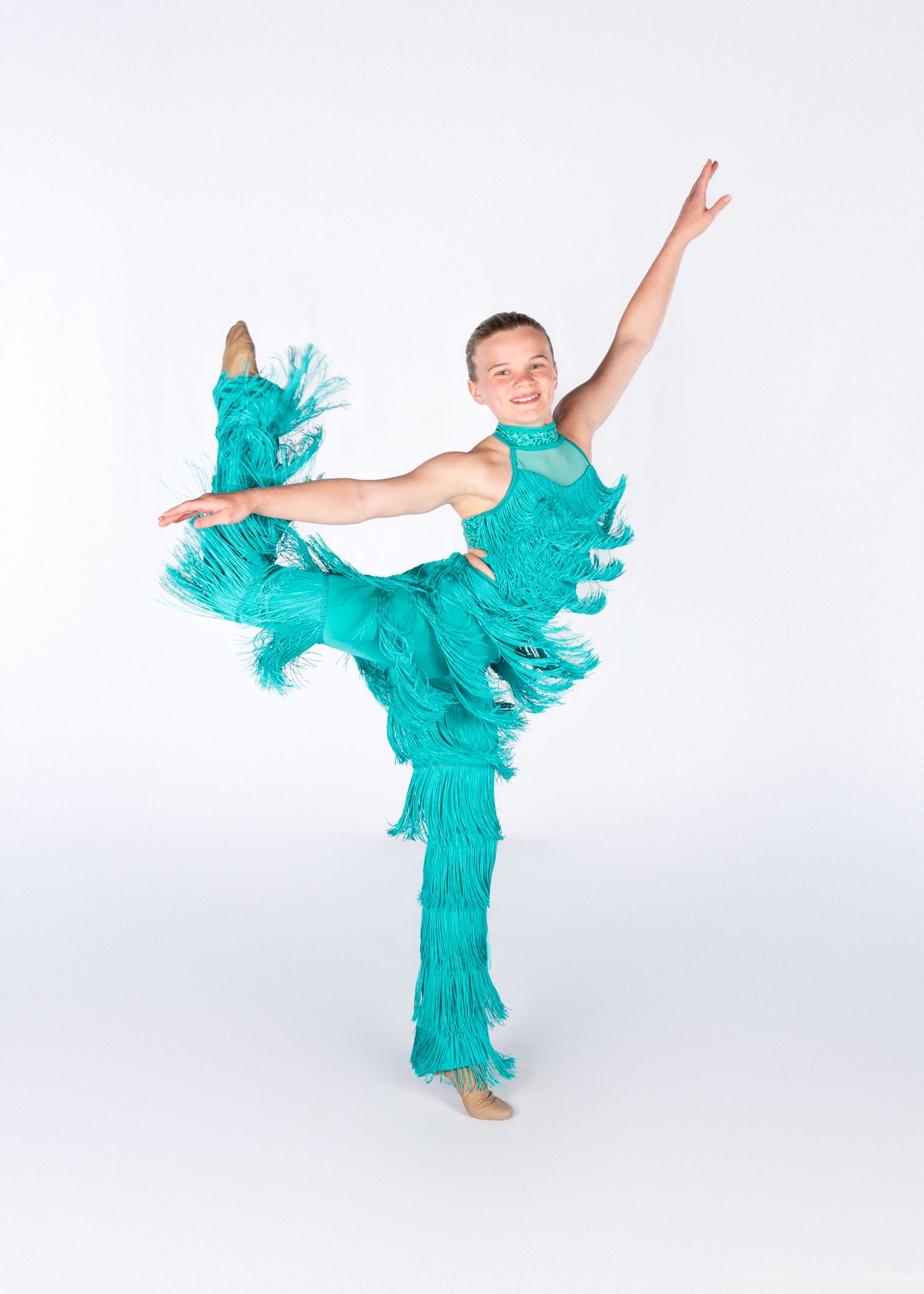 Dancer in turquoise fringe costume executes an elegant standing split pose with flowing movement.