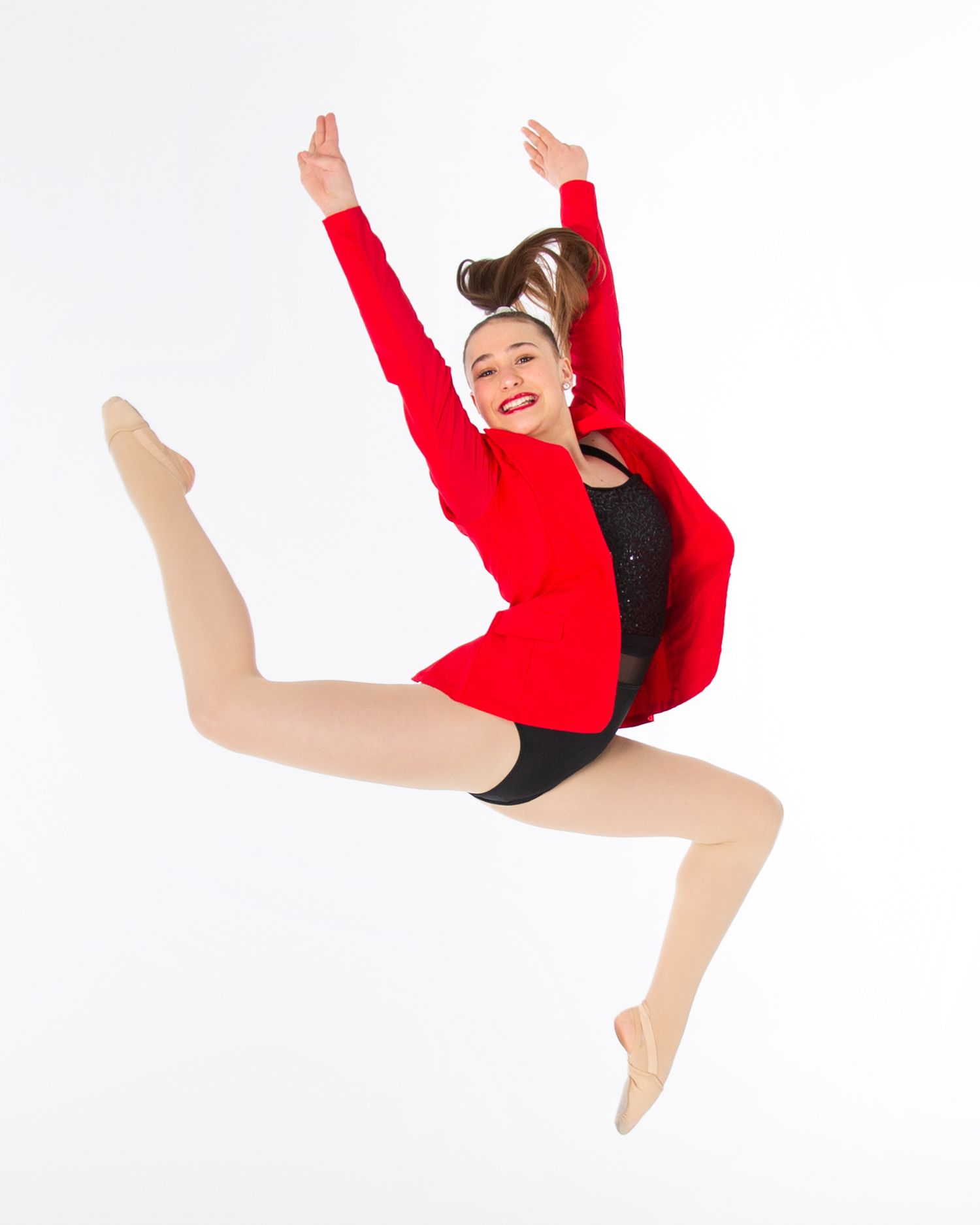 Dancer in red jacket and black leotard performs energetic split jump against white background.