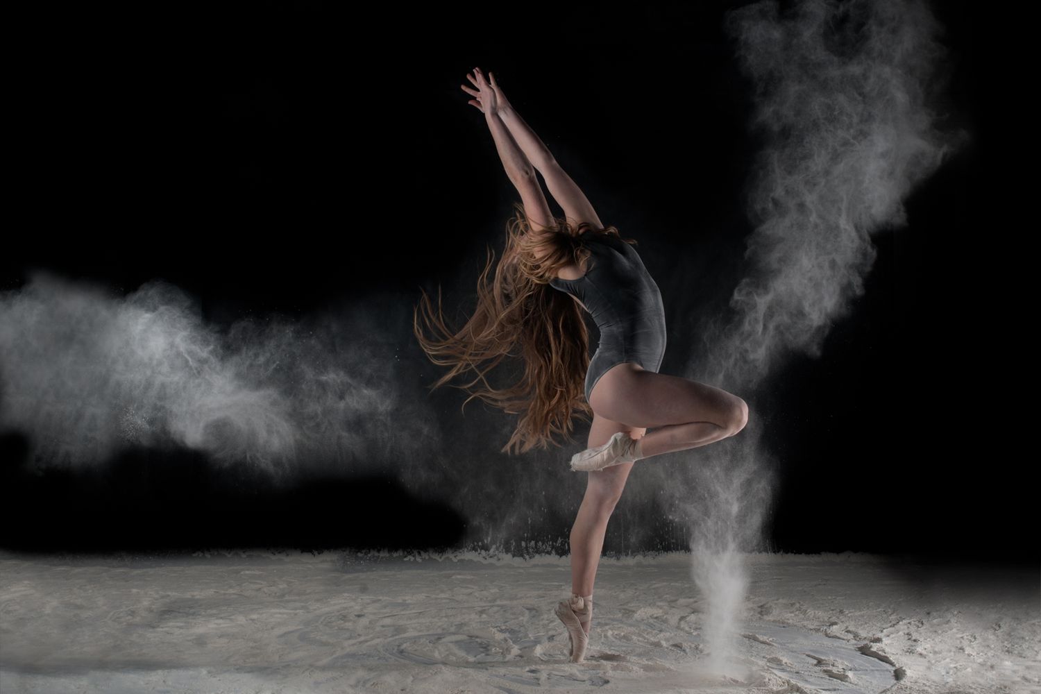 A dancer performs in a cloud of white powder against a dark background, creating a dramatic ethereal effect.