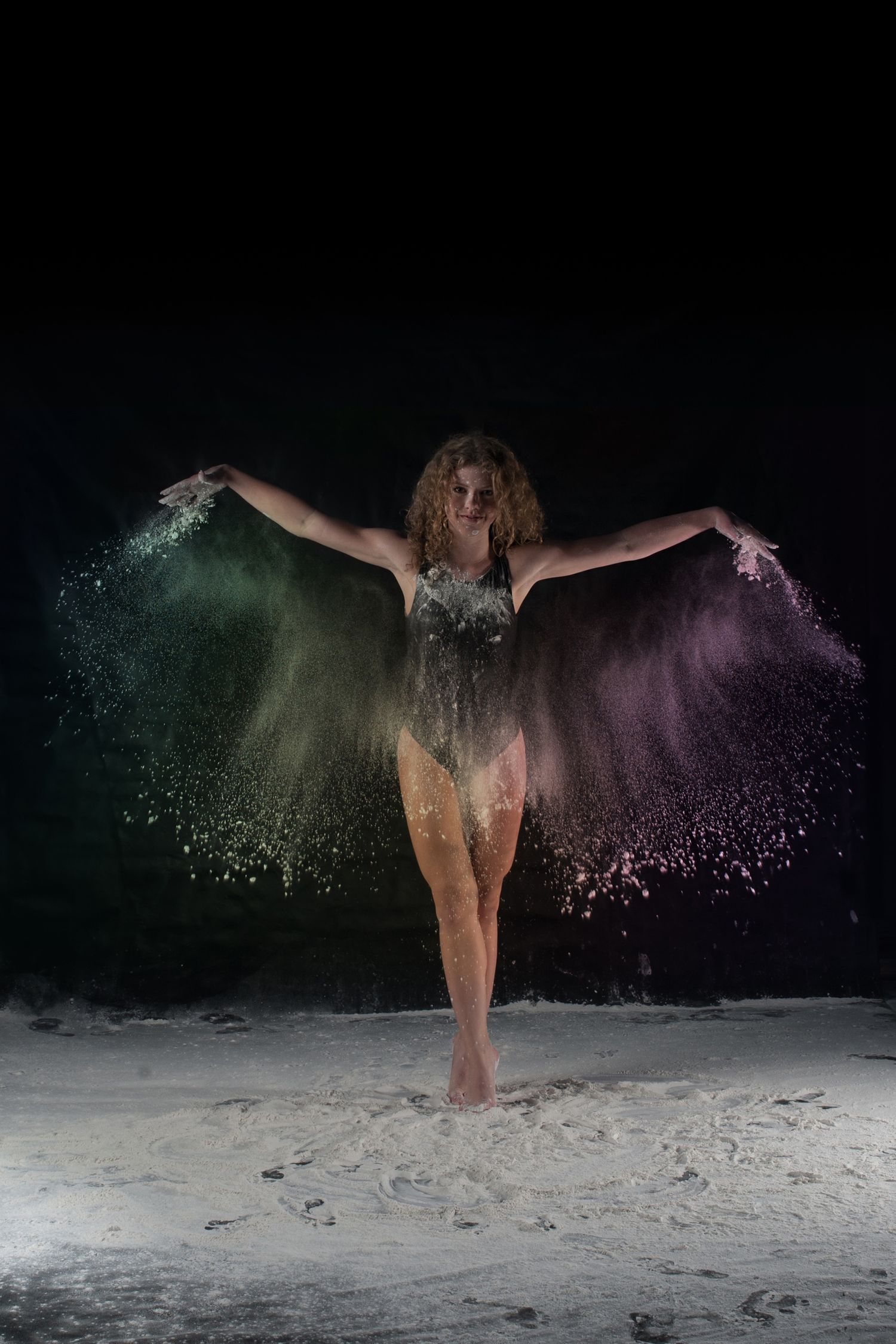 Dramatic dance pose with colorful powder effects creating ethereal silhouette against dark background.