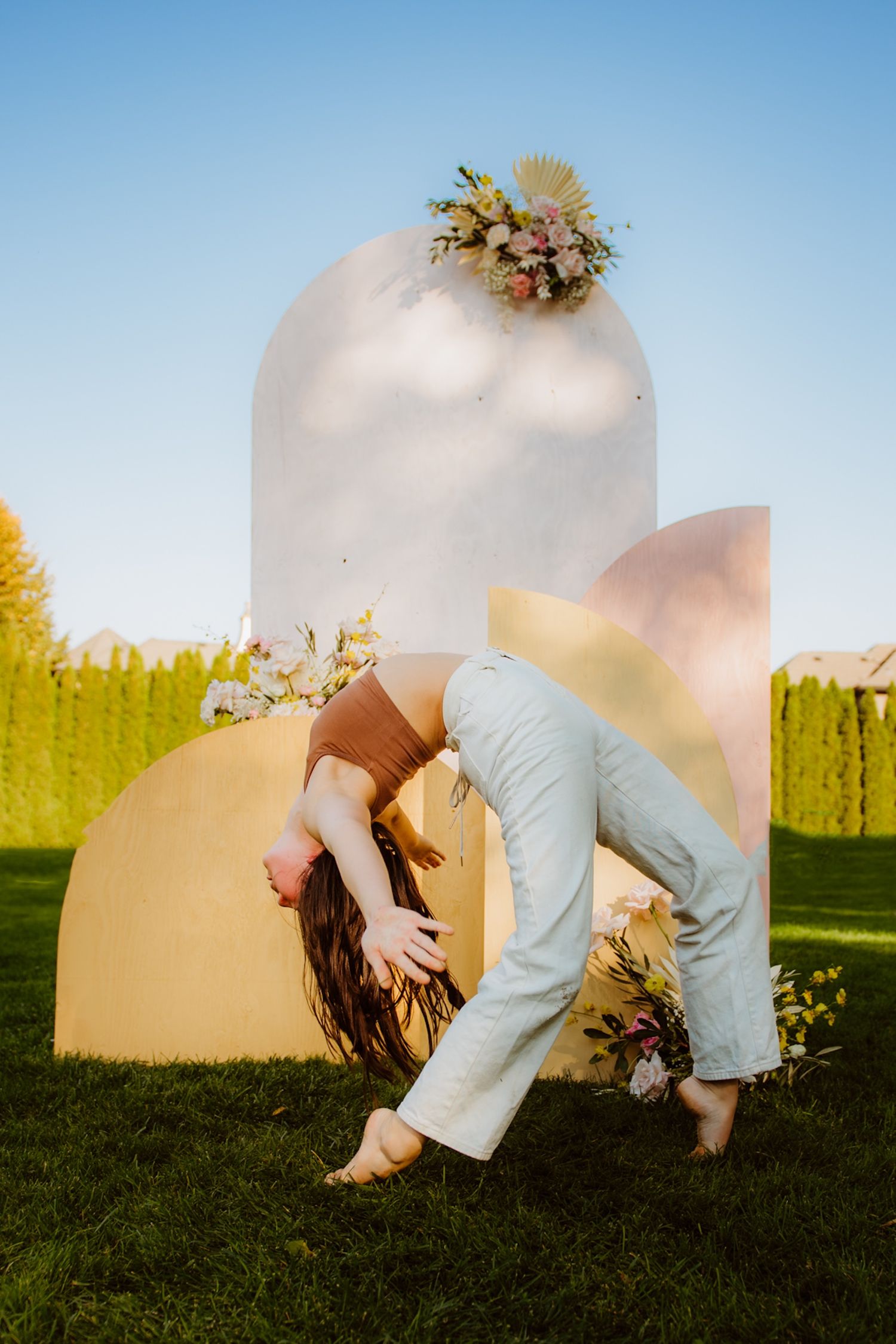 Artistic dance pose against geometric backdrop with floral elements in outdoor garden setting.