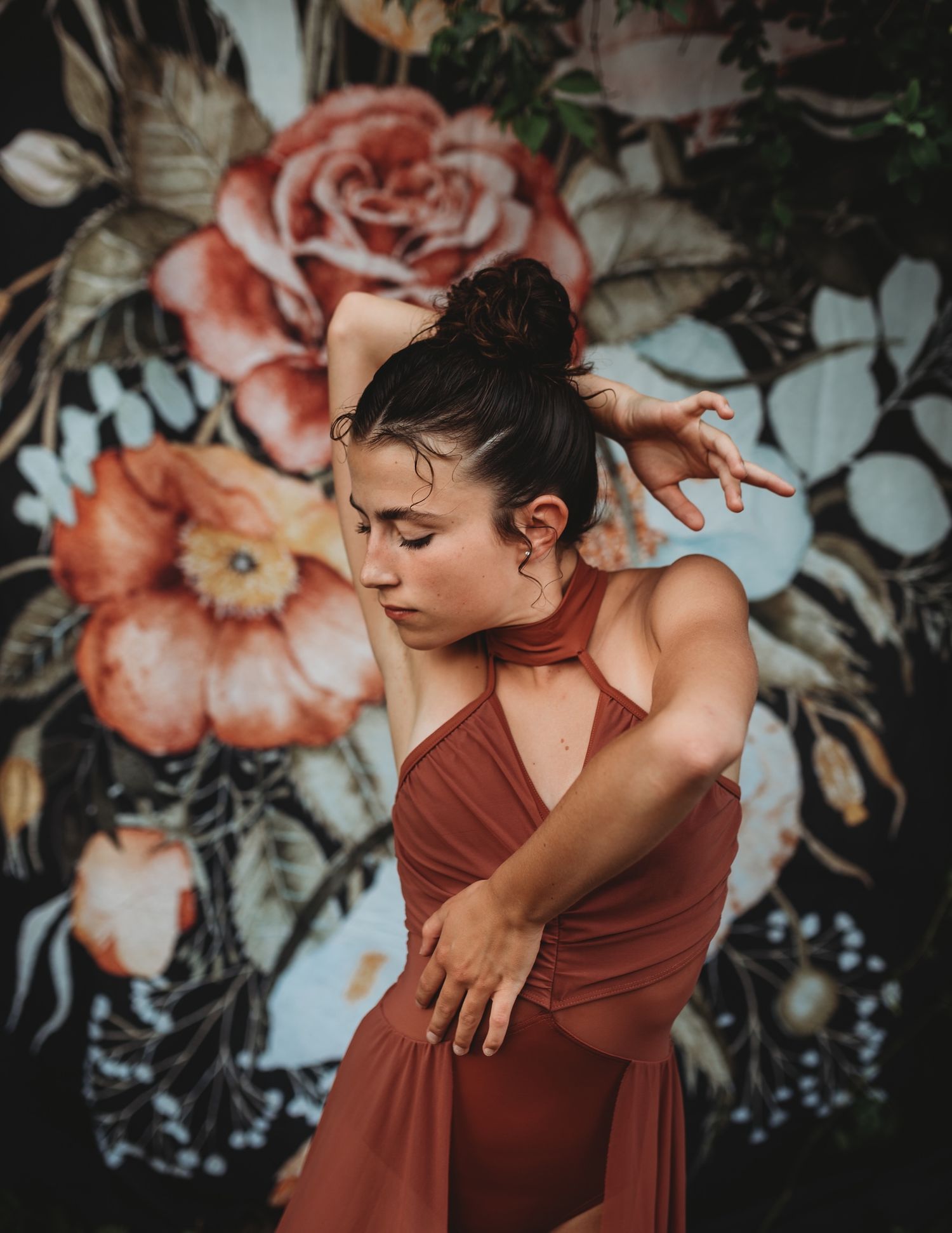 Expressive dance movement captured against a moody floral wallpaper background in warm earth tones.
