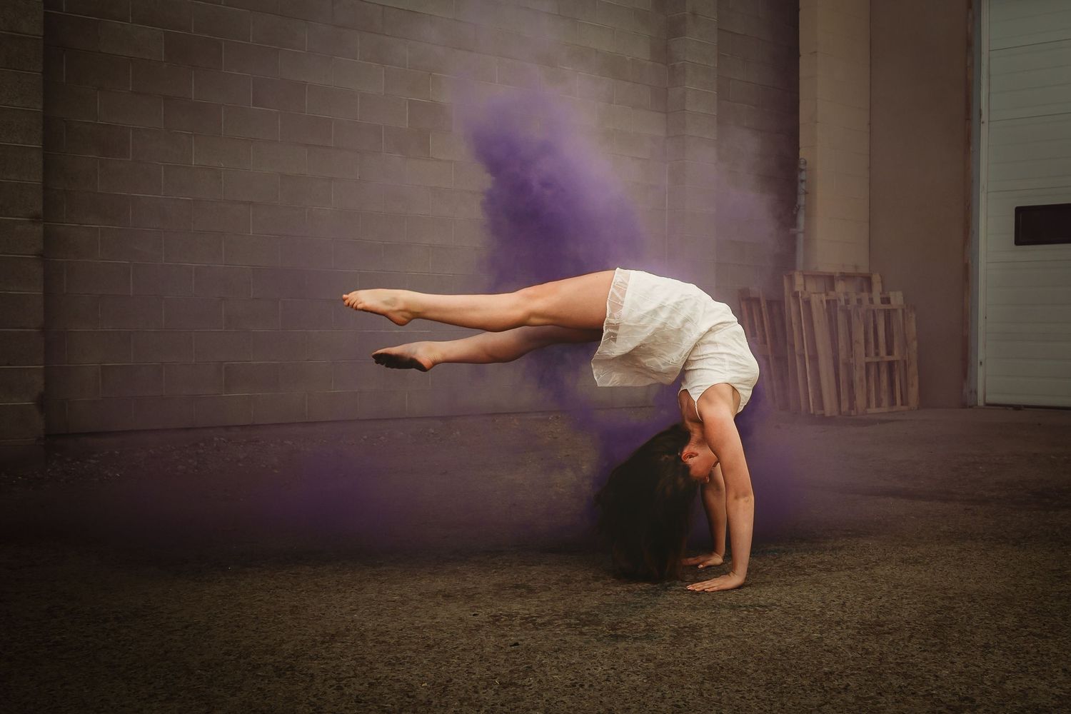 Athletic person performing a handstand with a purple smoke effect in a dark indoor setting.