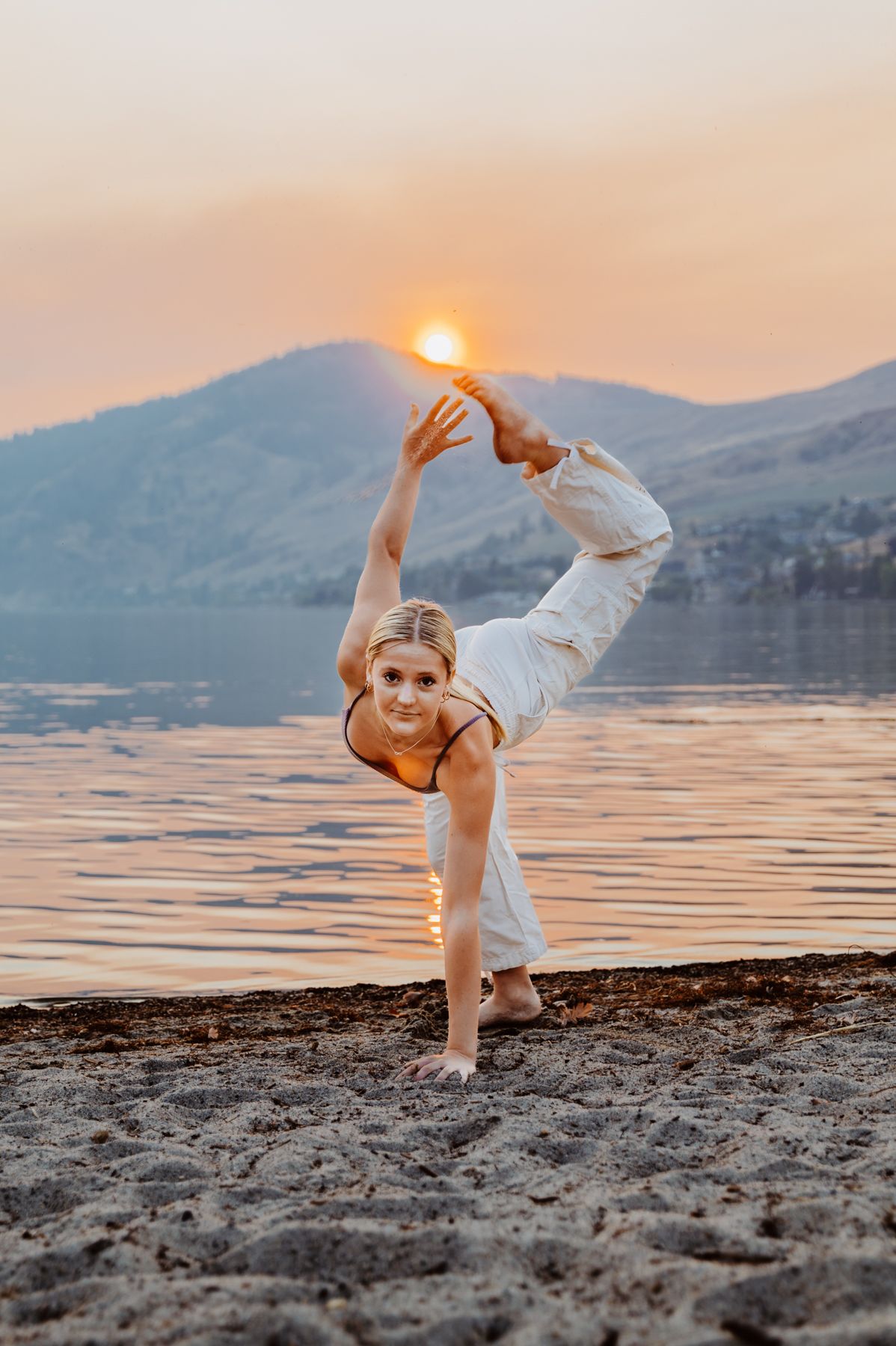 A person strikes a yoga pose against a mountain lake backdrop during golden sunset.