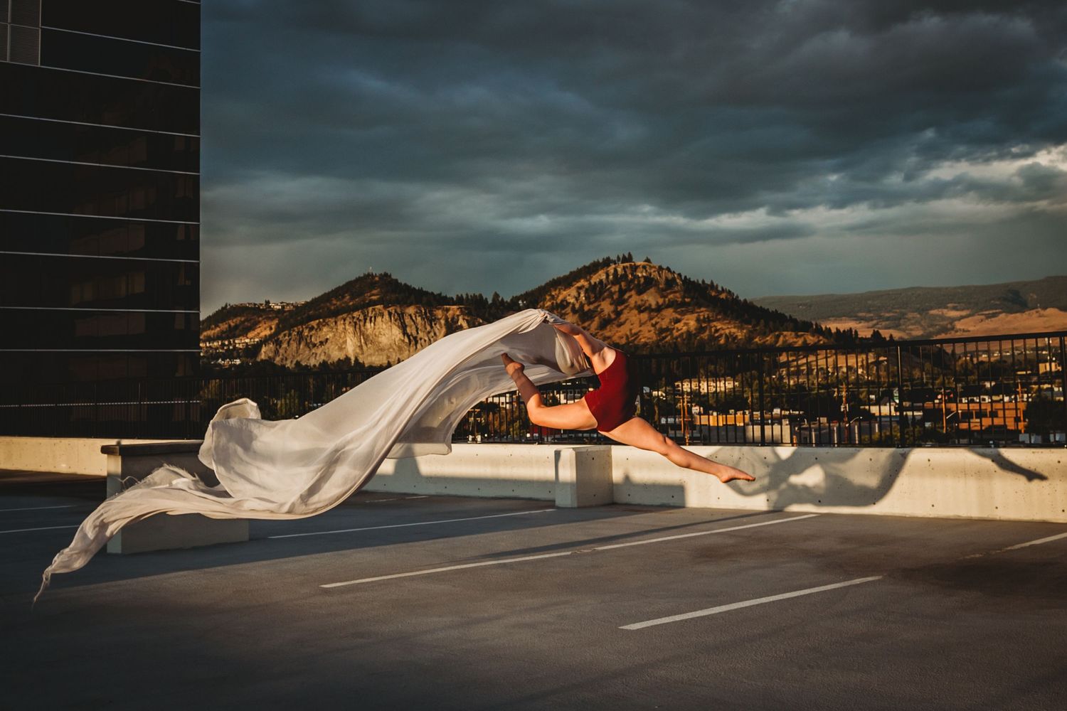 A flowing white dress billows dramatically against a stormy mountain backdrop during a rooftop photoshoot.