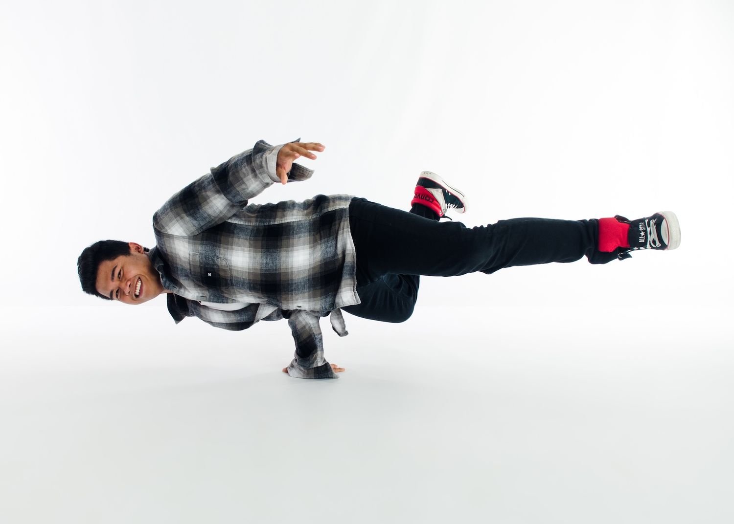 Break dancer performs freeze move wearing plaid shirt and black pants.