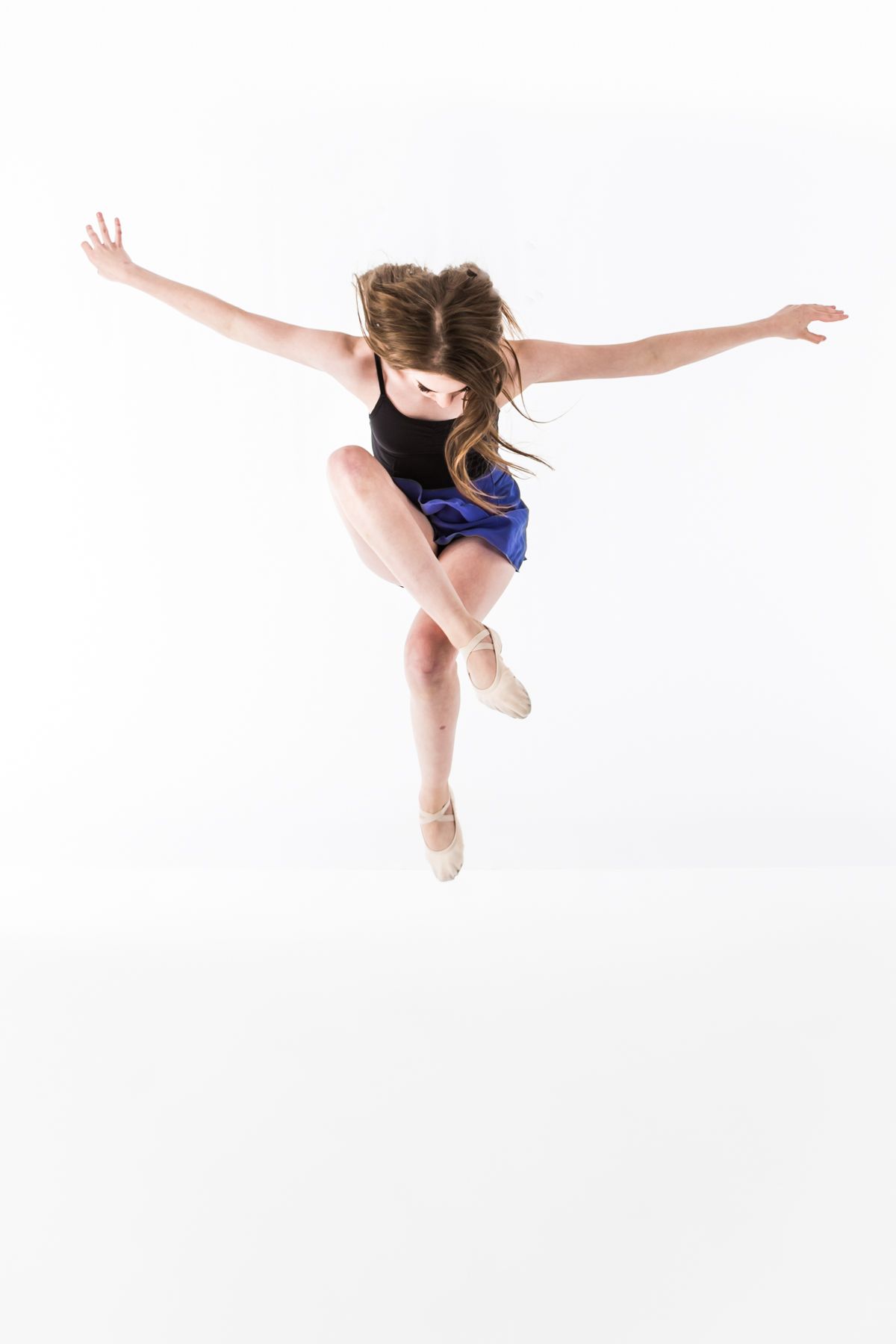Graceful dancer in blue leotard leaping through the air during contemporary dance performance.