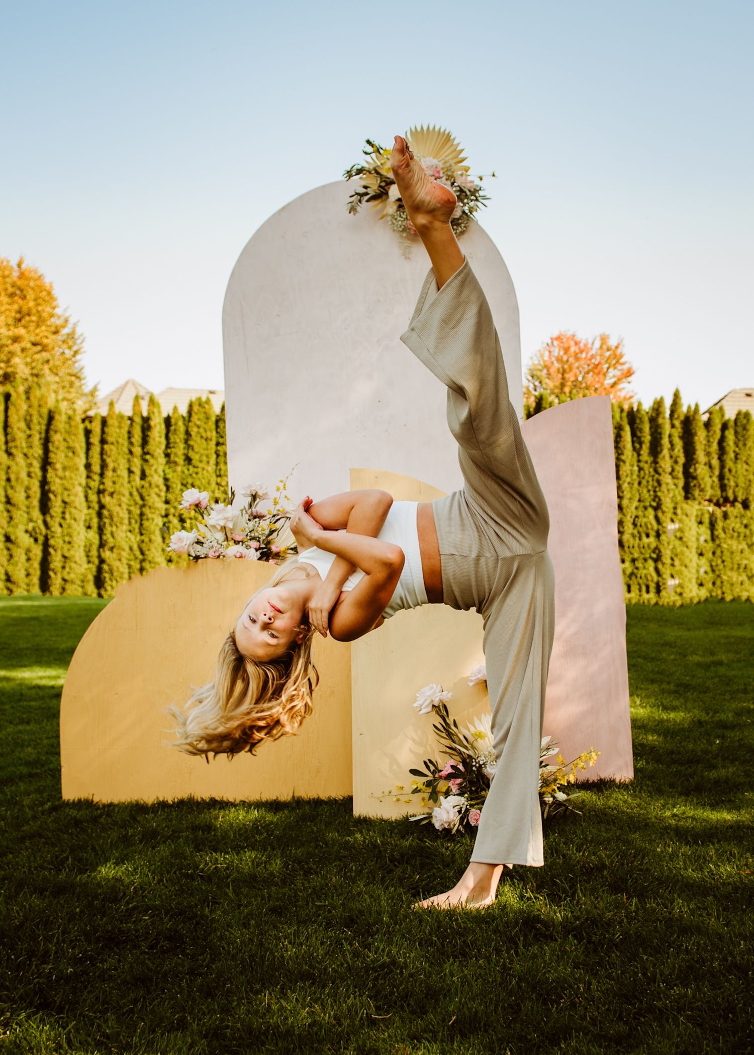 Contemporary dancer in flowing outfit performs inverted pose against curved architectural elements and hedges.