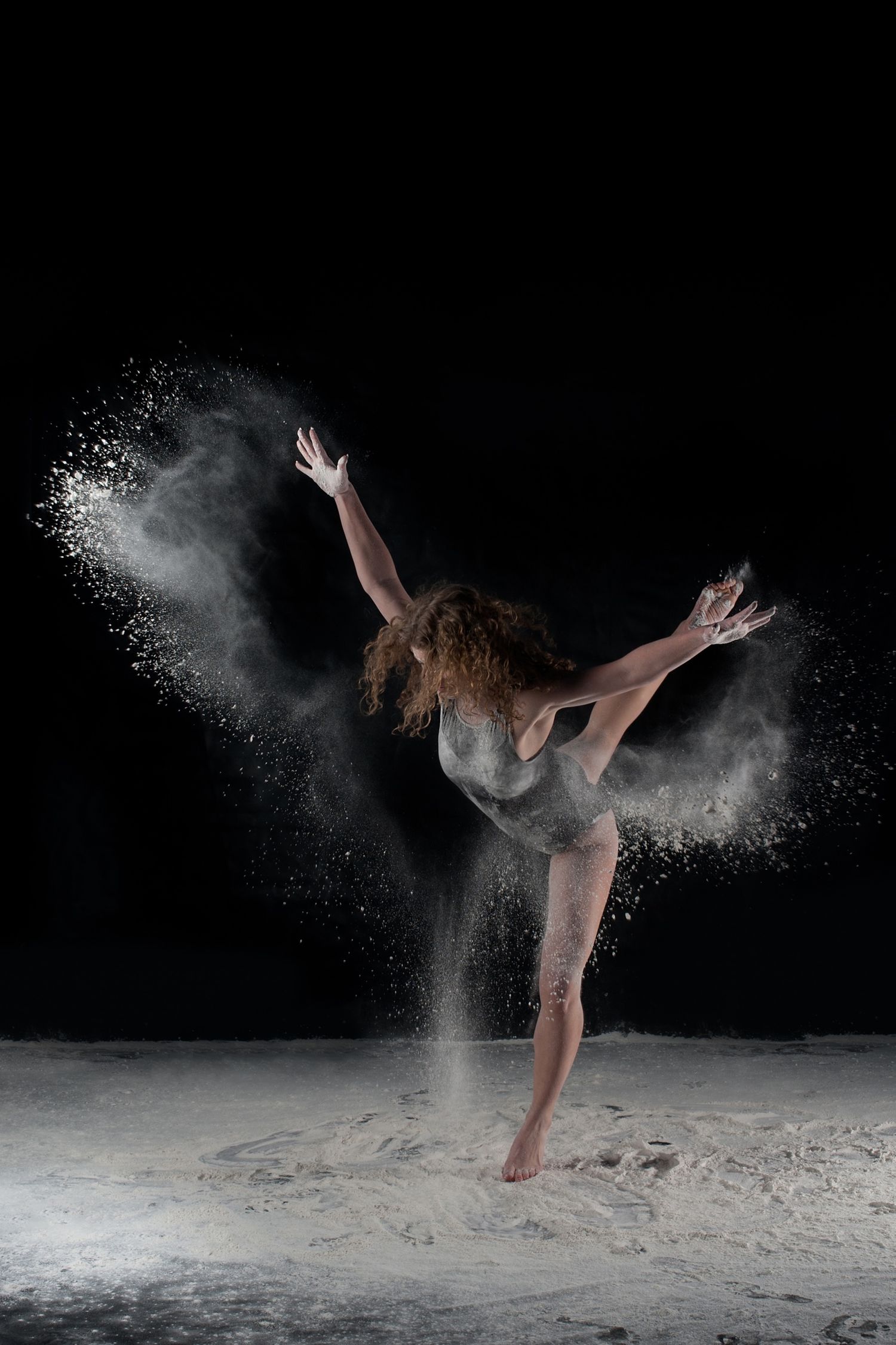 Contemporary dancer in graceful pose with white powder creating dynamic motion effect on black background.