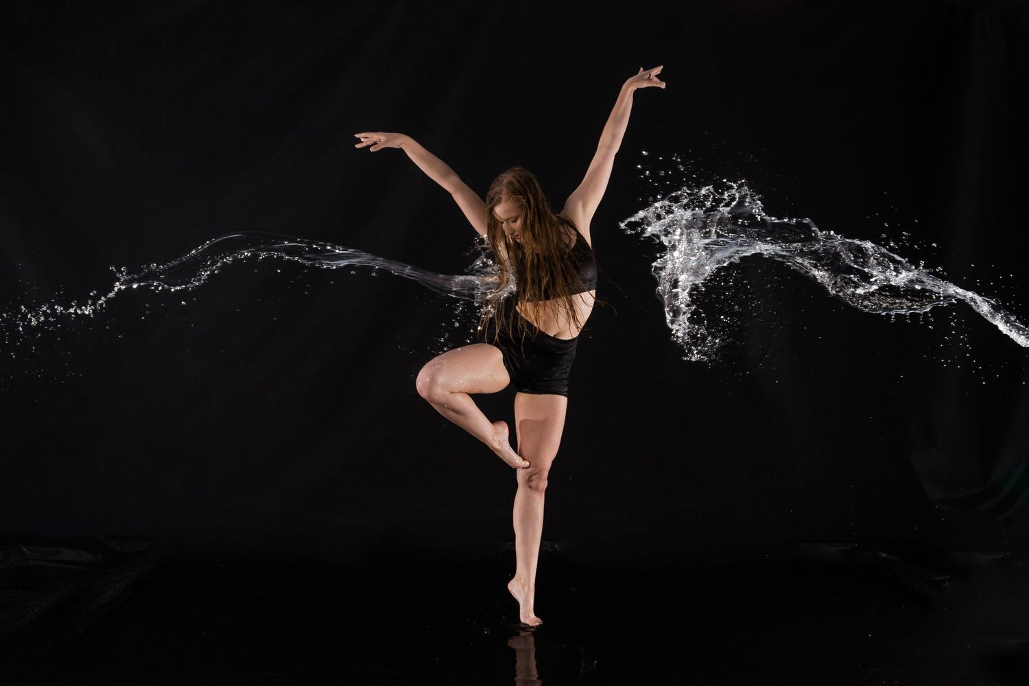 Dynamic dance figure silhouetted against black backdrop with symmetric water streams creating wings effect.