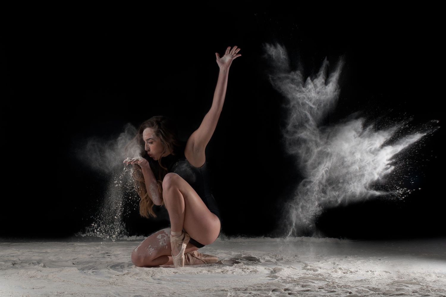 A dancer performing on the floor with white powder creating dramatic movement effects against a black background.