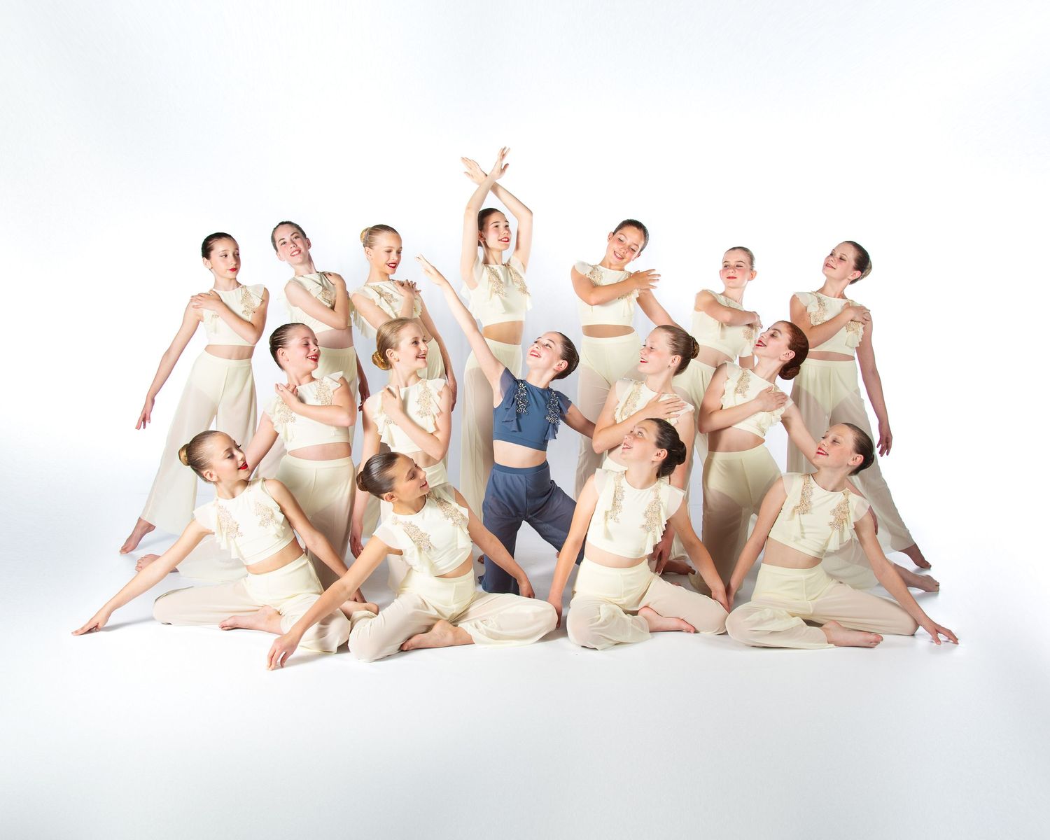 Dancers in cream-colored costumes perform elegant poses in a contemporary dance ensemble against a white backdrop.