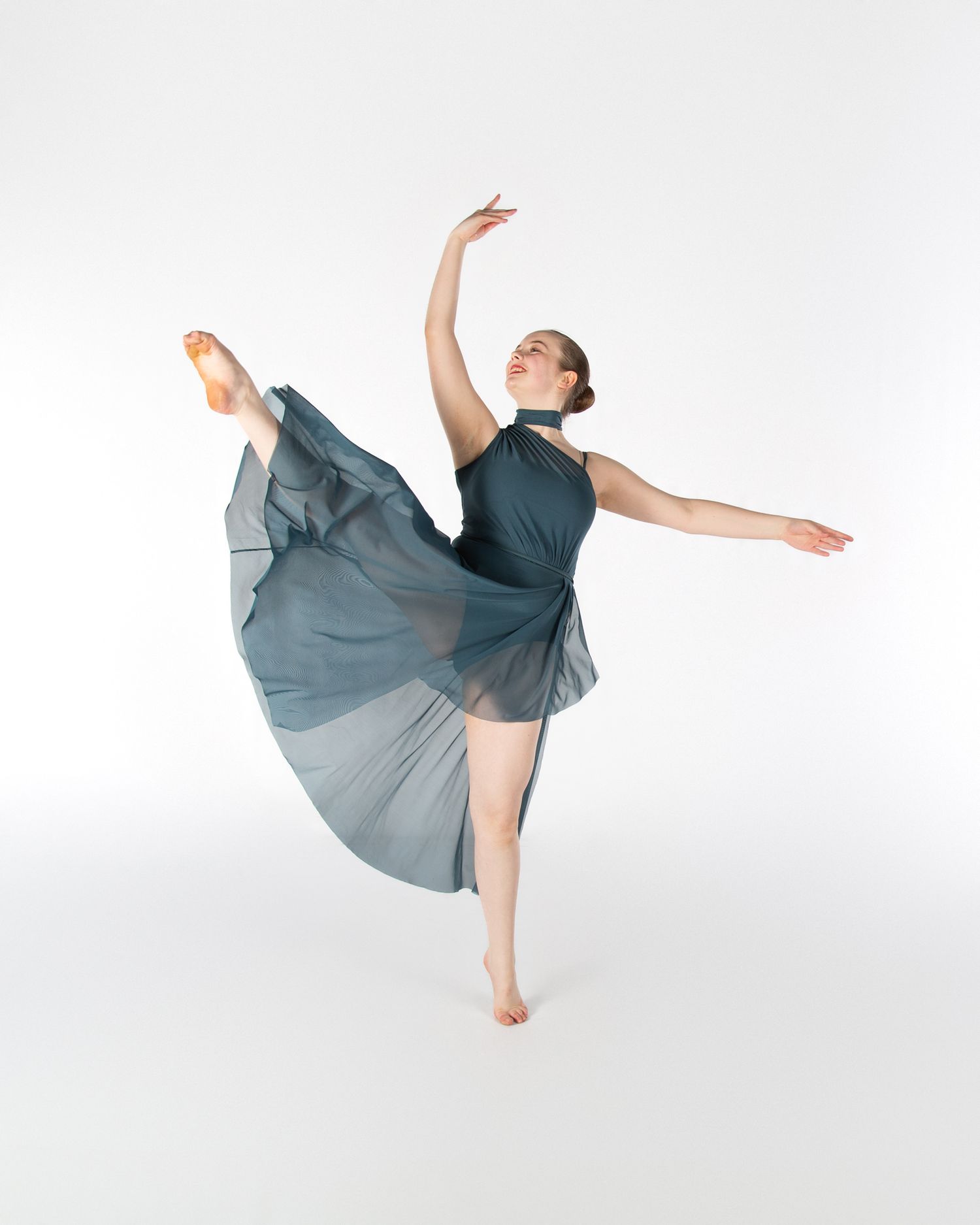 Graceful dancer in grey dress performing an arabesque position against white background.