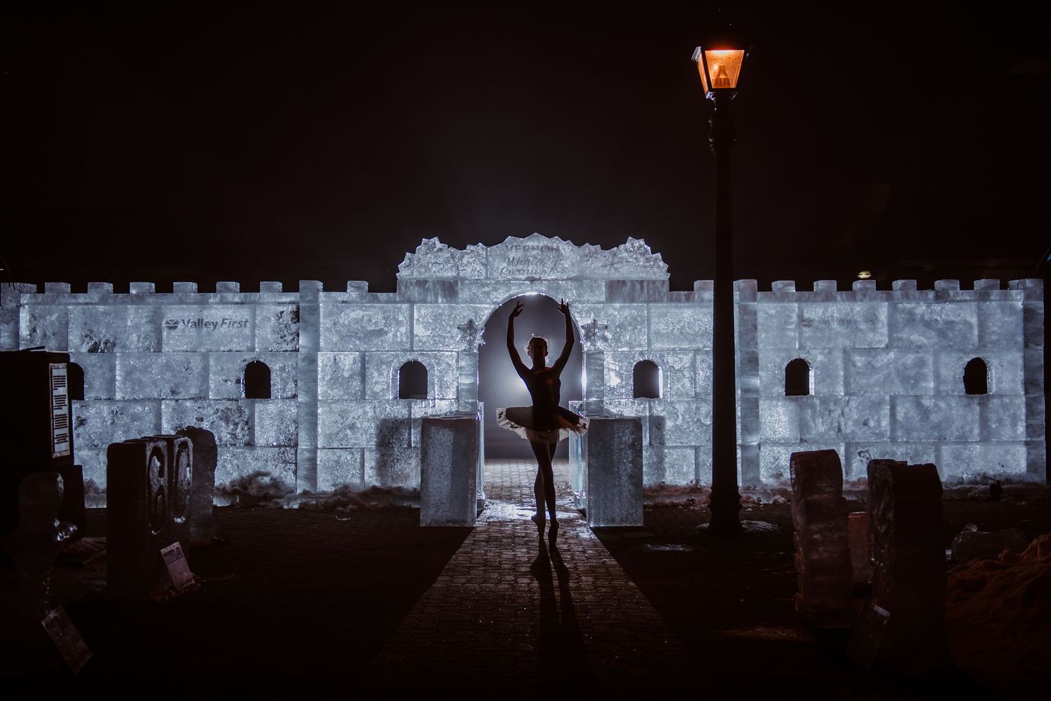 Silhouette of a dancer striking a graceful pose against illuminated stone castle walls at night.