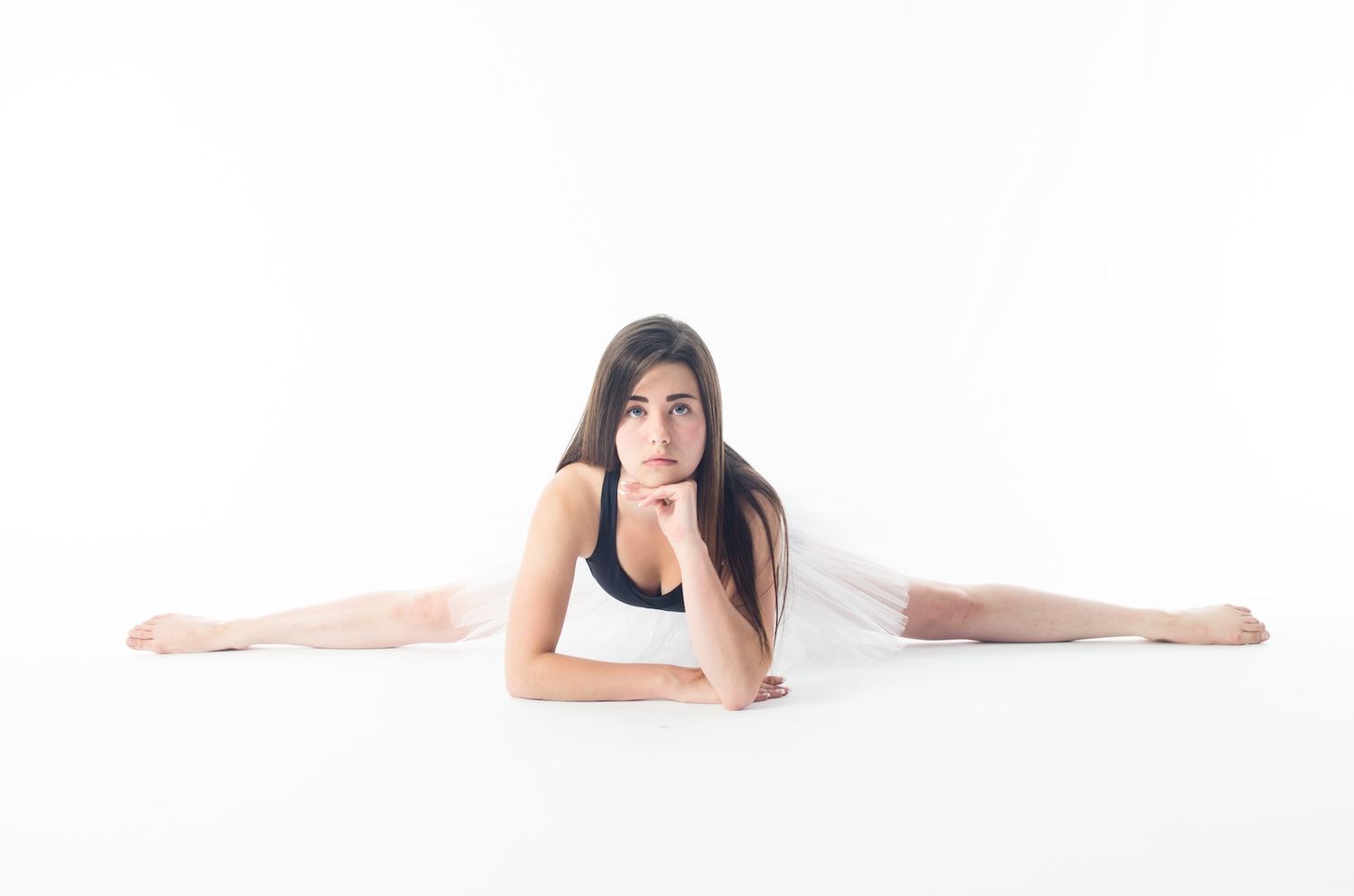 Person in white athletic wear performs full split stretch position on white background.