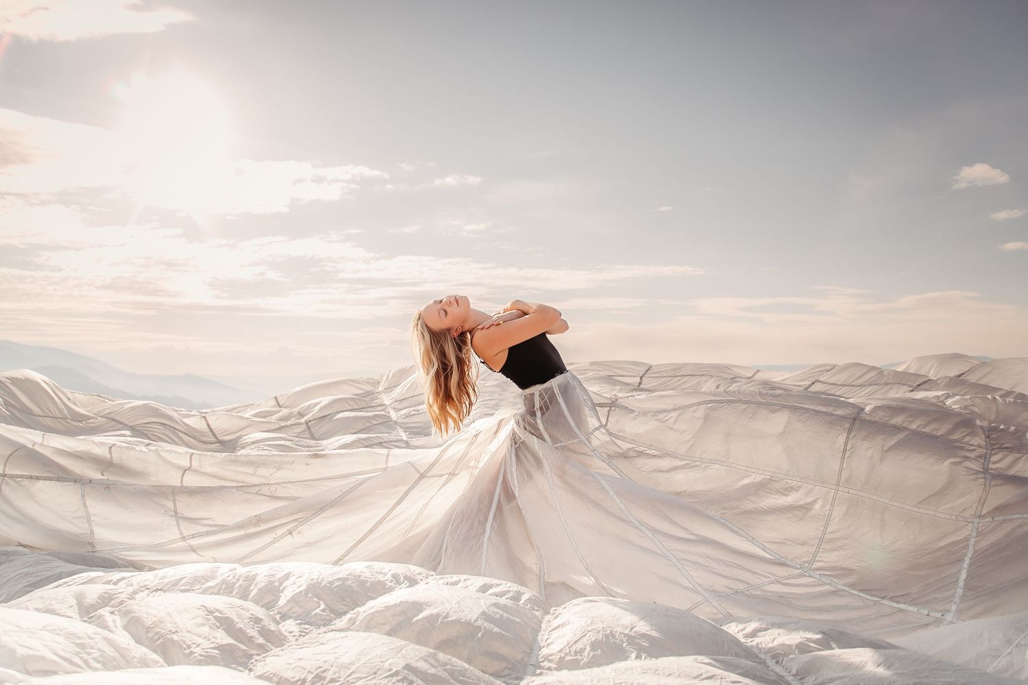 Ethereal white fabric flows across a dreamy landscape as a figure emerges from beneath the billowing material.