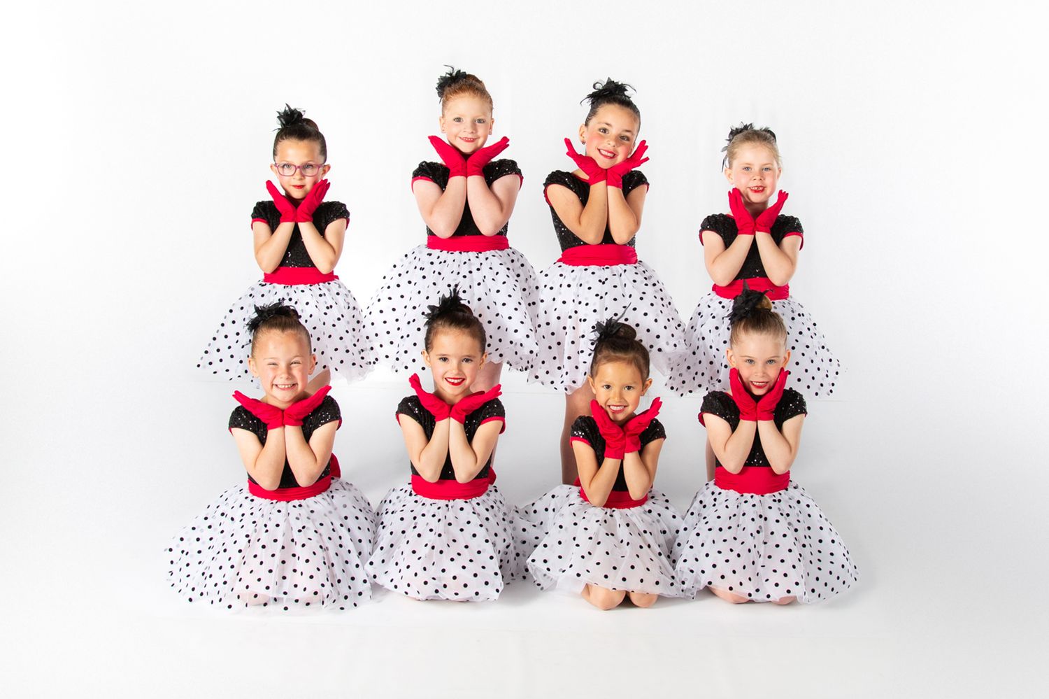 Eight young dancers in polka dot skirts and red tops pose in two rows for a dance recital photo.