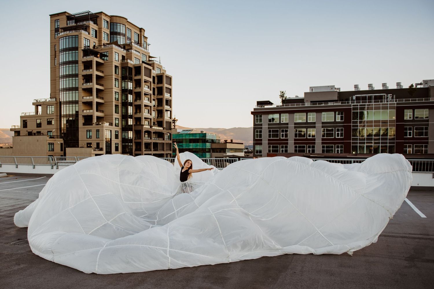 A person sits on a large inflated white plastic structure on a rooftop with urban buildings in the background.