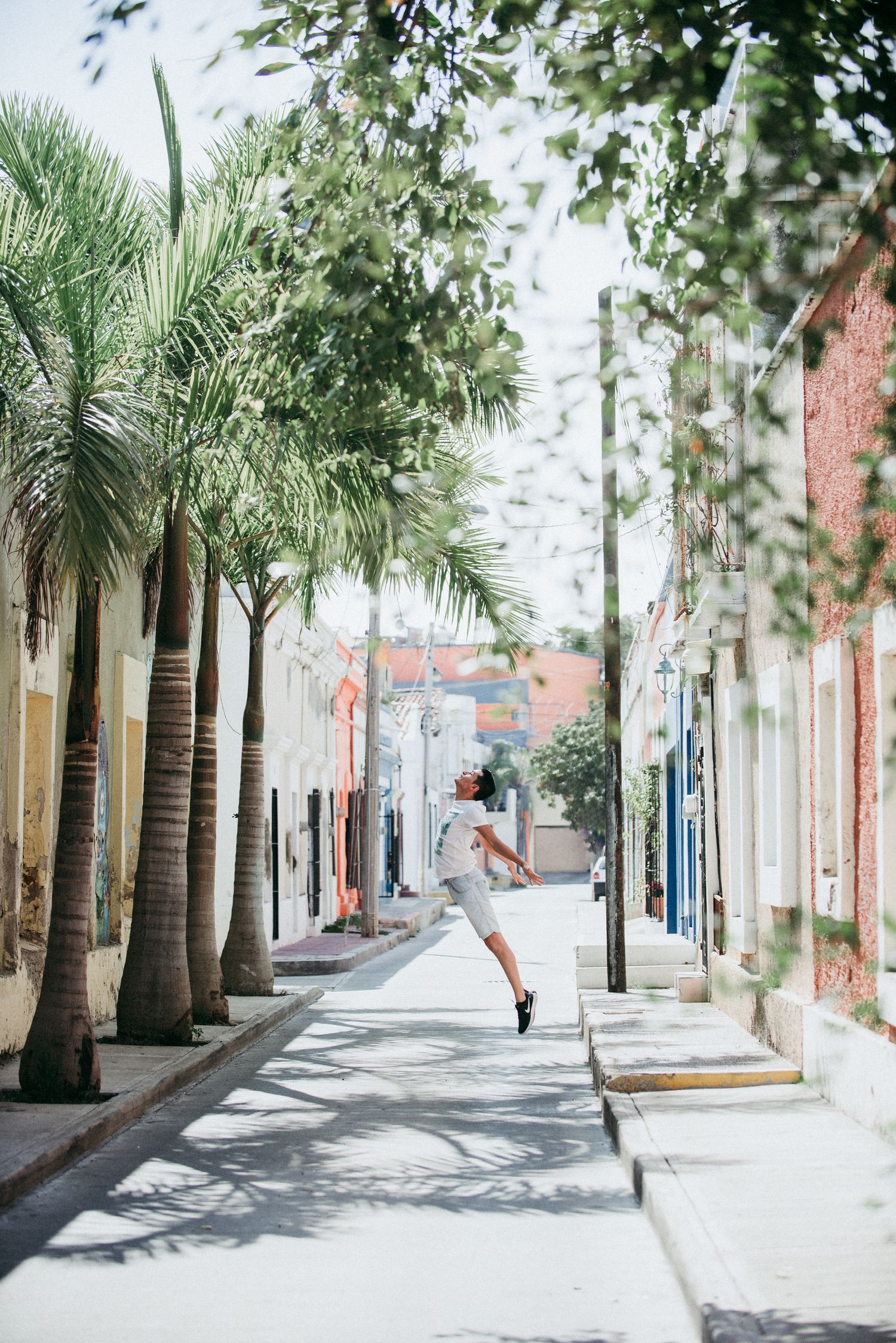 A figure leaps joyfully on a palm tree-lined street with colorful buildings in Charleston, South Carolina.