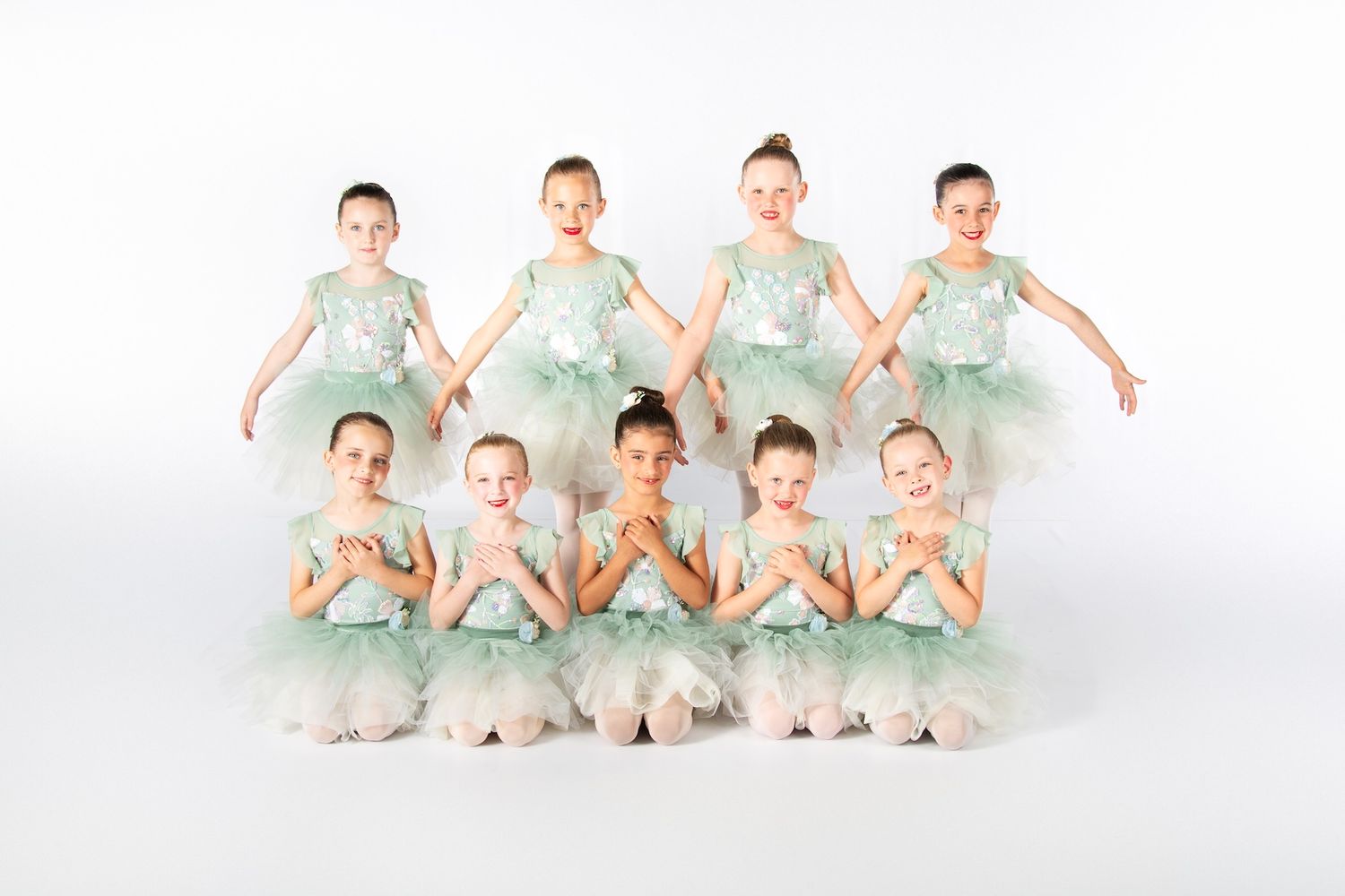 Young dancers in mint green tutus pose in two rows for group portrait.