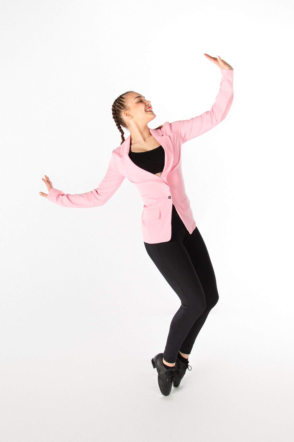 Dancer in pink blazer and black pants performs expressive movement against white background.