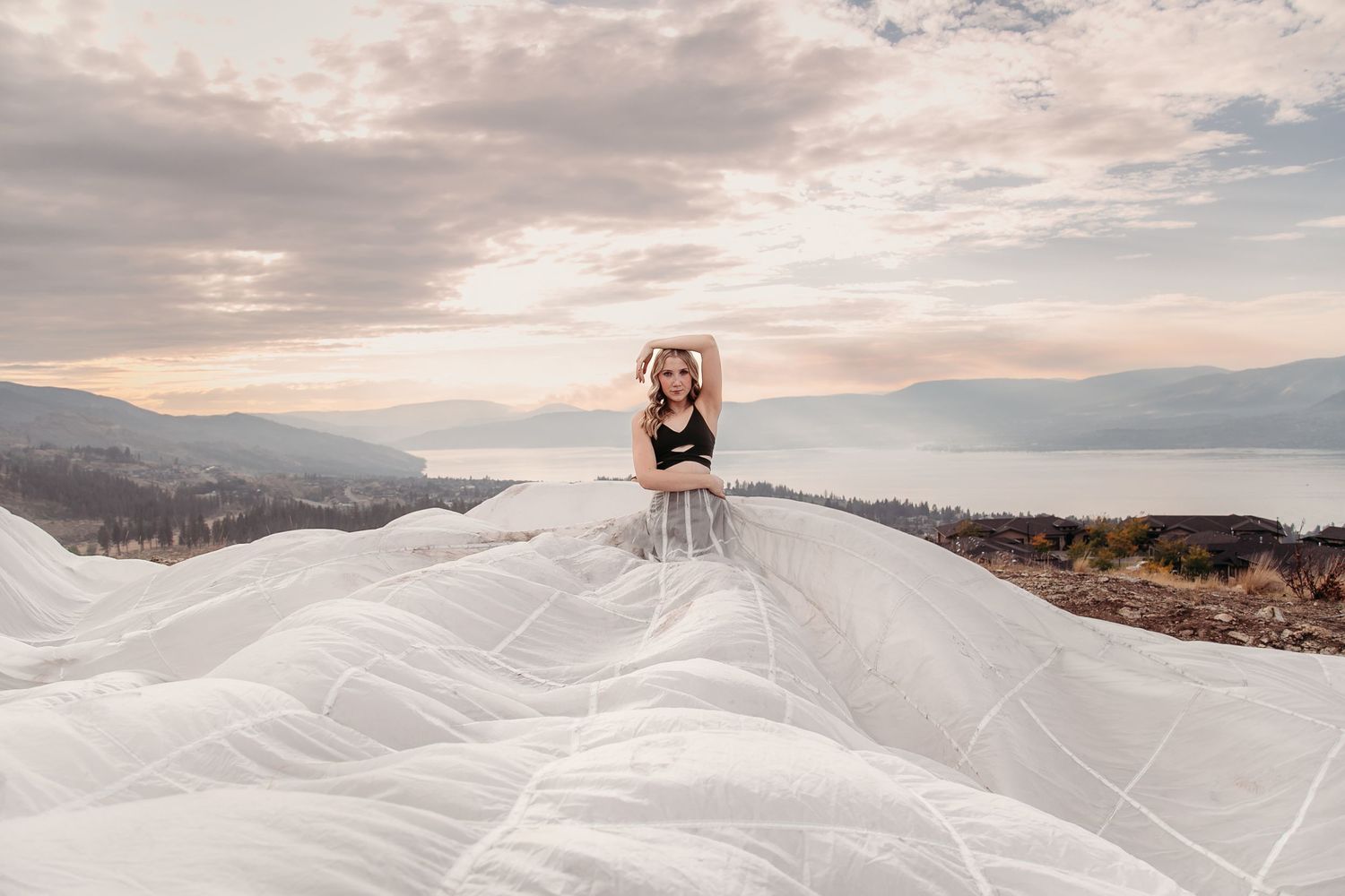 A flowing white dress billows dramatically against a scenic mountain landscape at sunset.