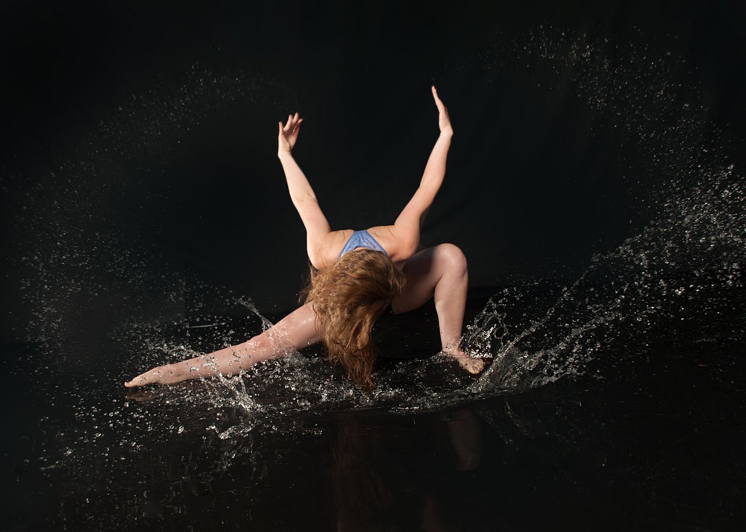 Artistic dance photography captures performer in dramatic pose with water splashing against dark background.