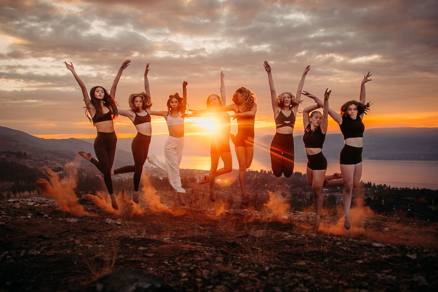 Silhouettes jumping against a dramatic sunset sky over mountain landscape.
