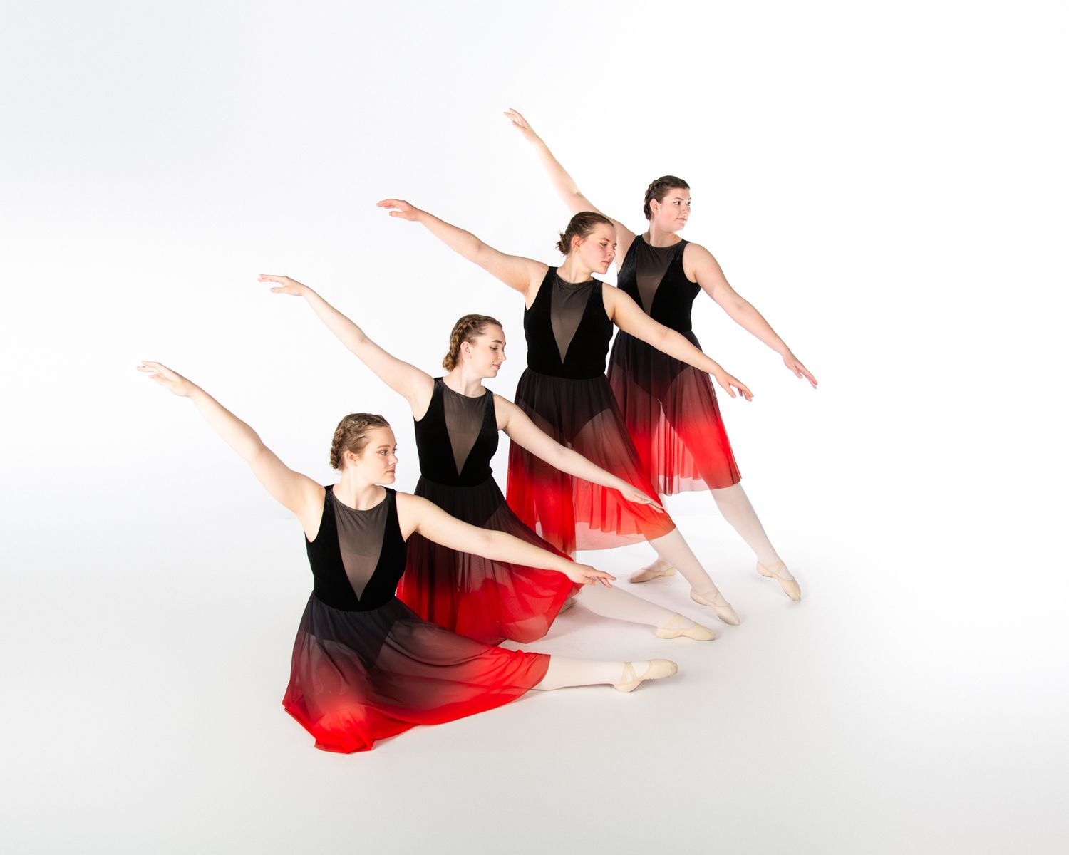 Dancers in black and red ombre dresses perform synchronized arabesque poses against white backdrop.