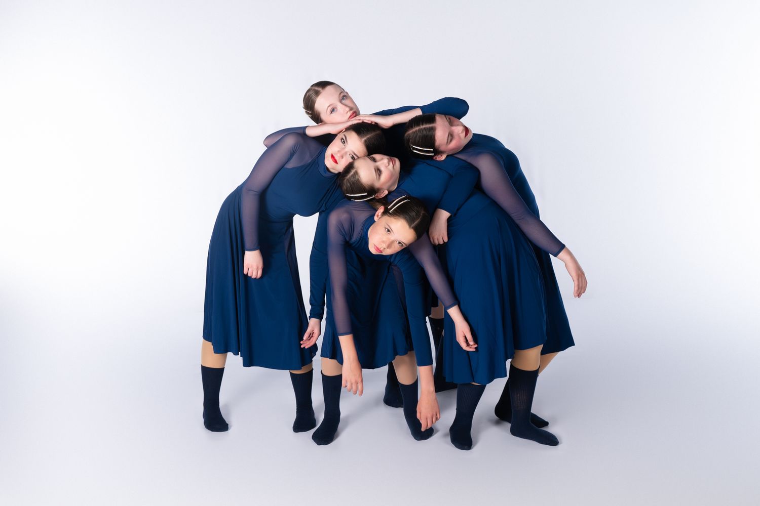 Dancers in navy blue costumes perform artistic group pose against white background.