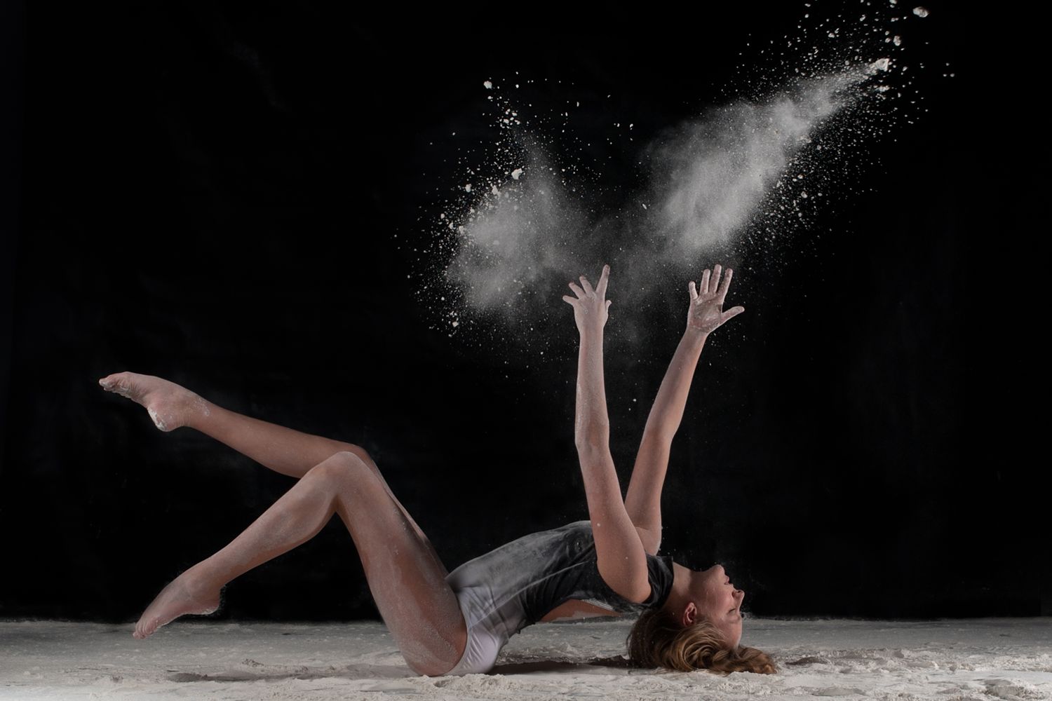 Dancer lying on floor surrounded by white powder creating dramatic effect during artistic performance.
