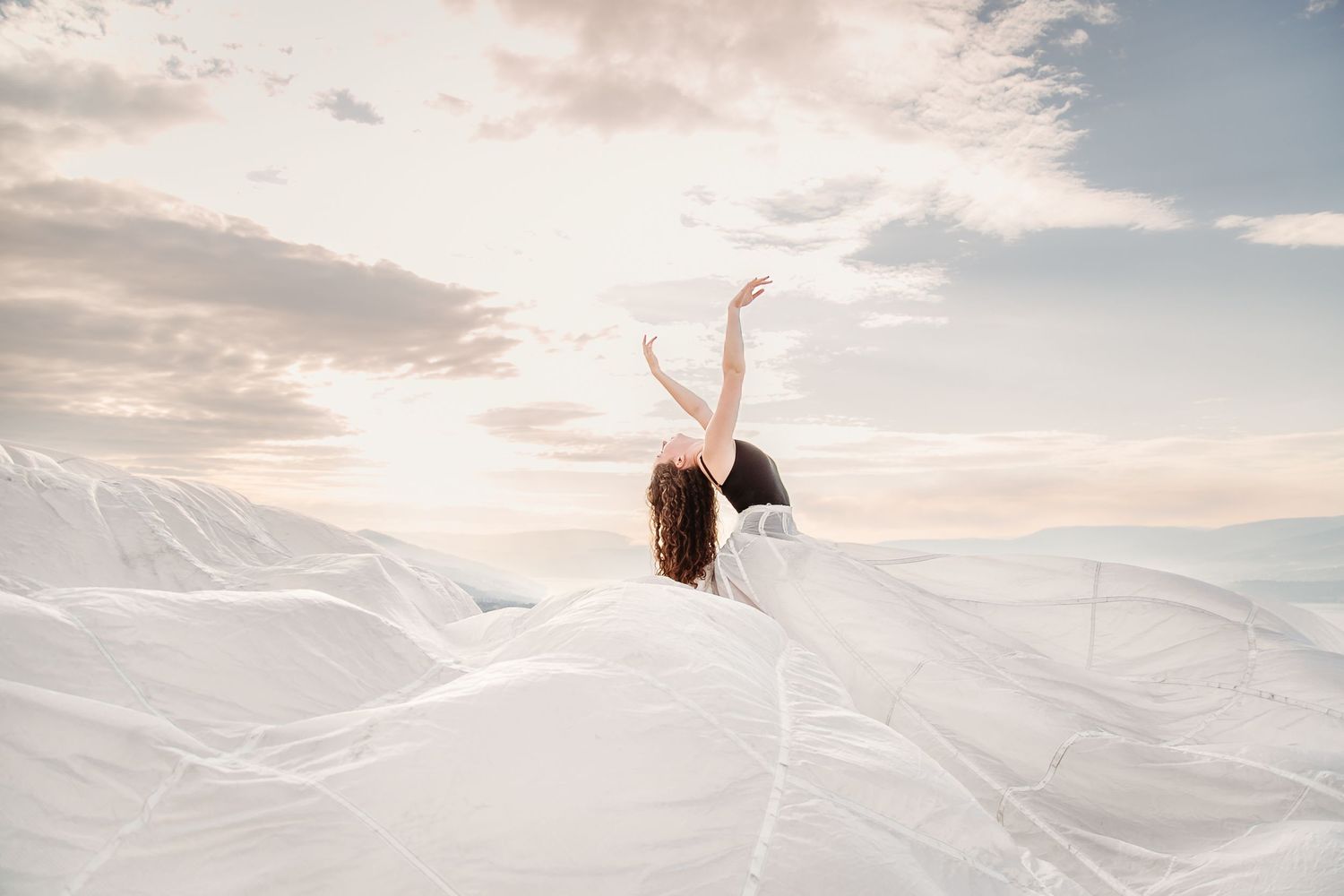 A dreamy ethereal shot showing a person emerging through billowing white fabric against snowy mountains at sunset.