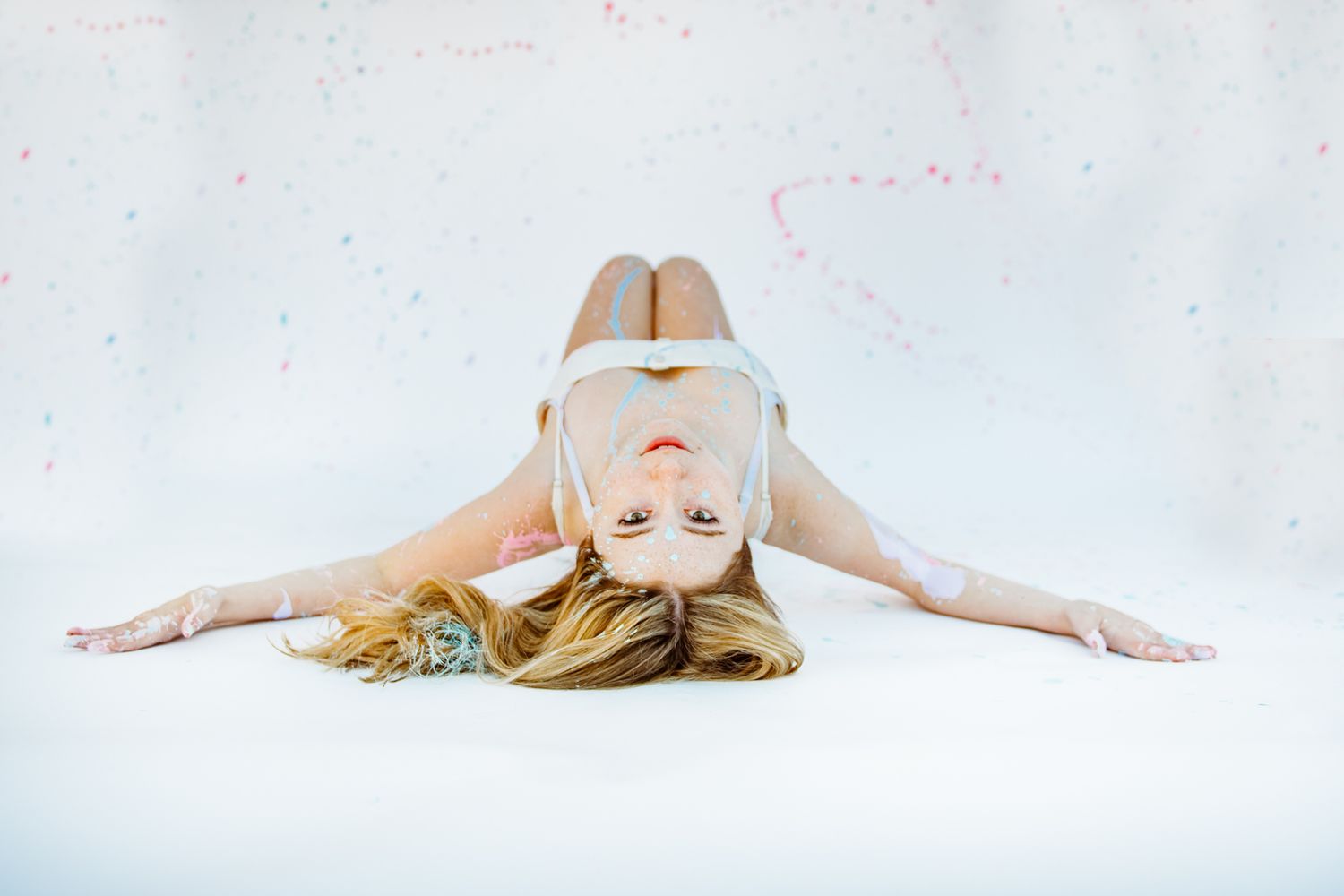 Woman in white dance attire lying on her back in an artistic pose on white studio floor.
