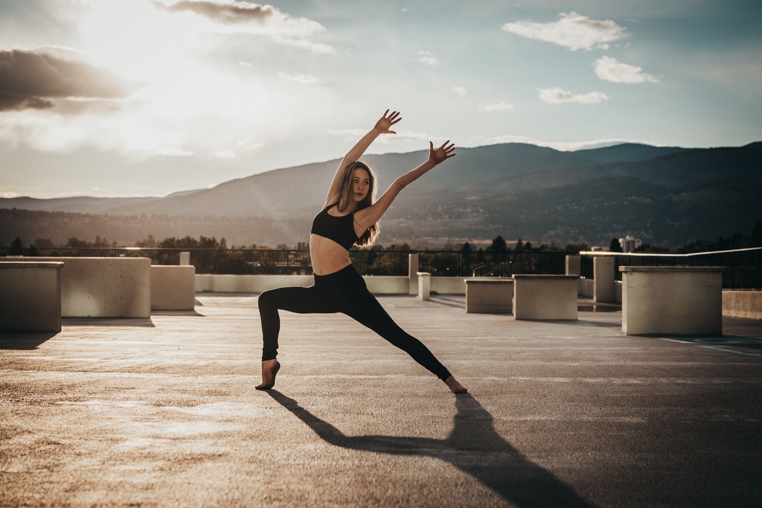 Athletic woman practicing yoga on a rooftop at sunset with mountains in the background.