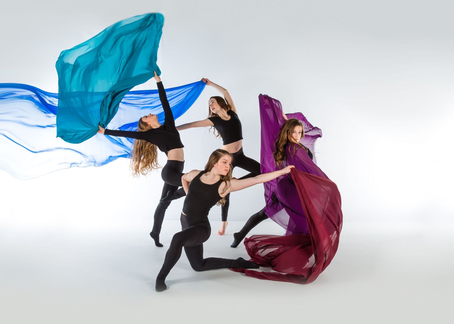 Contemporary dancers performing dynamic movements with flowing blue and purple fabric against a light background.