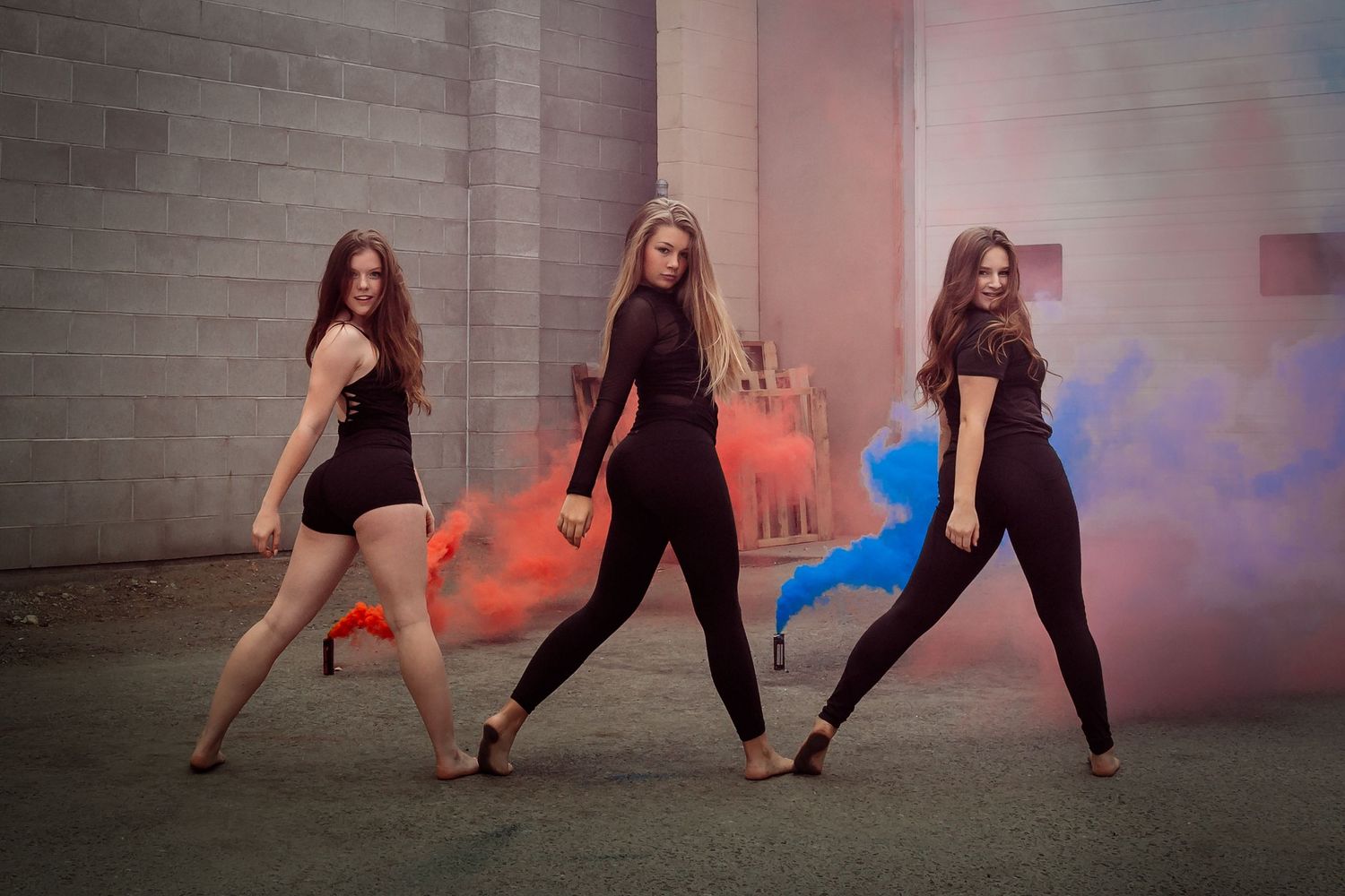 Three dancers in black outfits strike dynamic poses against a wall with colorful smoke effects.