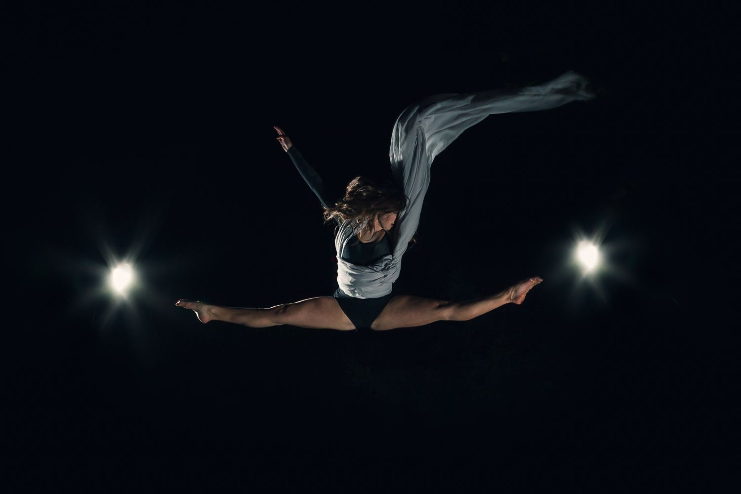 Dramatic silhouette of a dancer performing a split leap against a dark backdrop with bright spotlights.