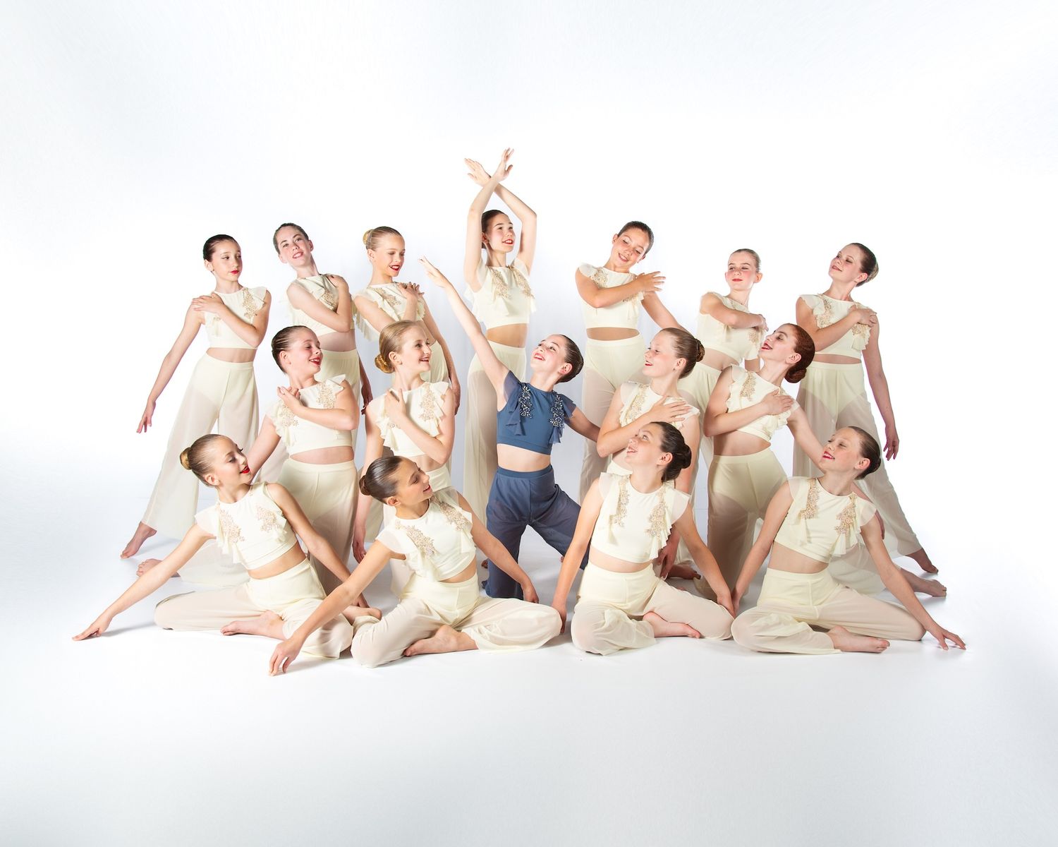 Ballet dancers in cream colored costumes strike graceful poses together in a contemporary dance formation on white.