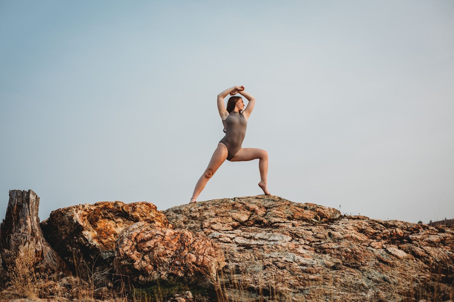Athletic pose performed on rocky mountain outcrop against blue sky.