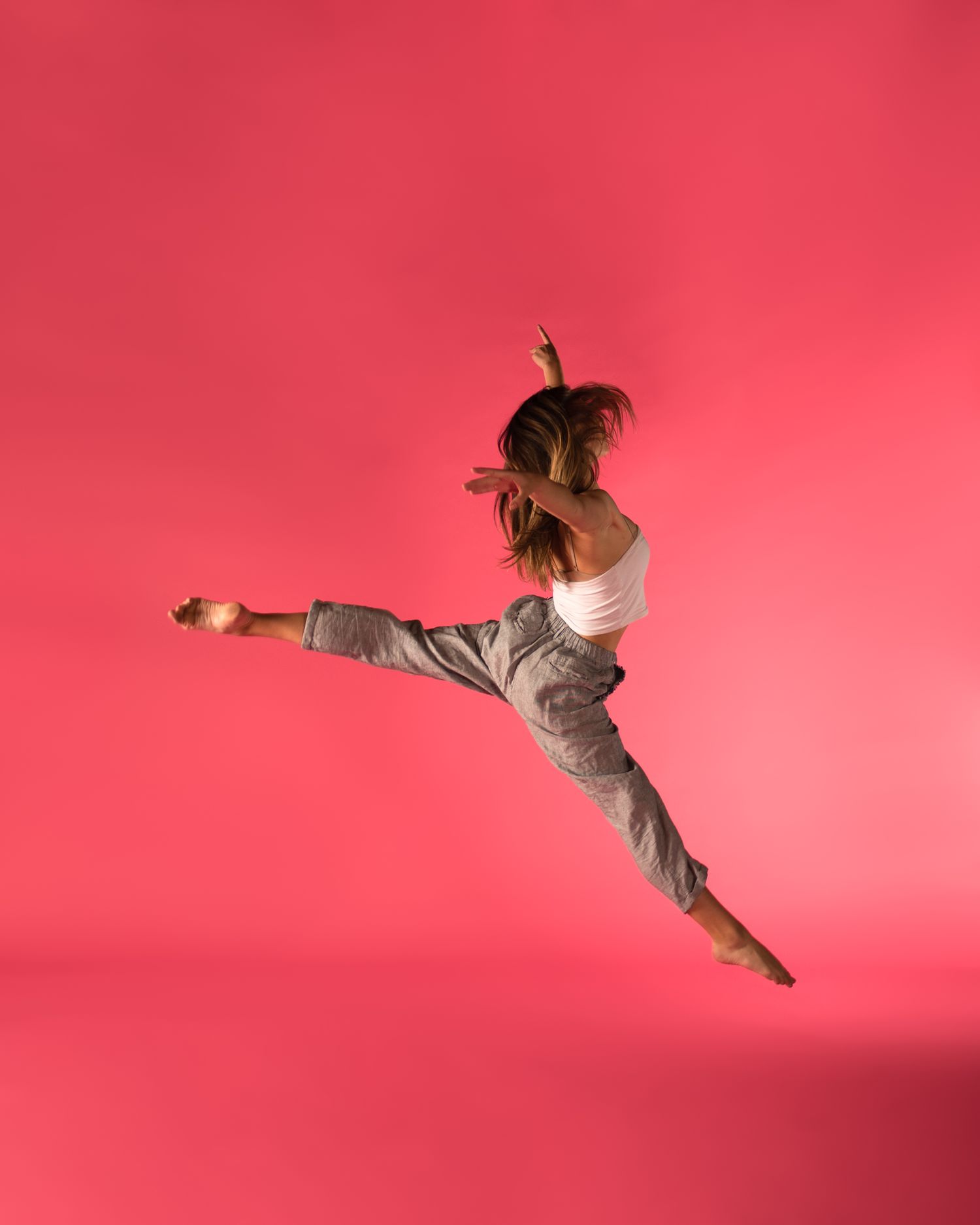 A dancer performs a dramatic leap with outstretched leg against a vibrant pink backdrop.