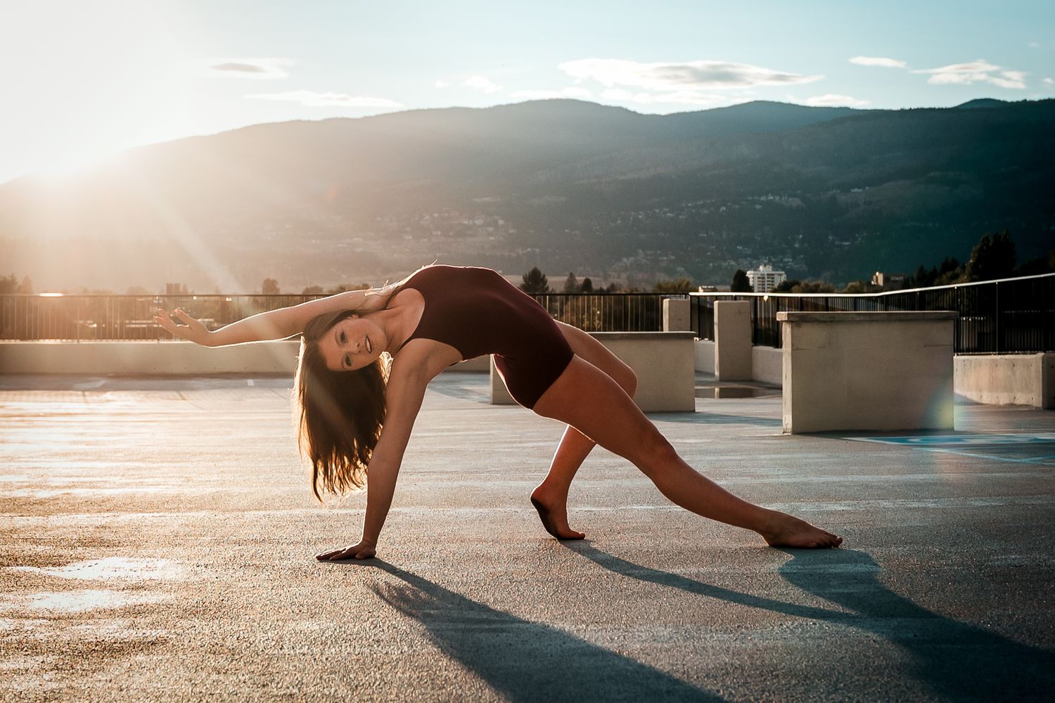 A dancer performs a graceful backbend pose on a rooftop at sunset with mountains in the background.