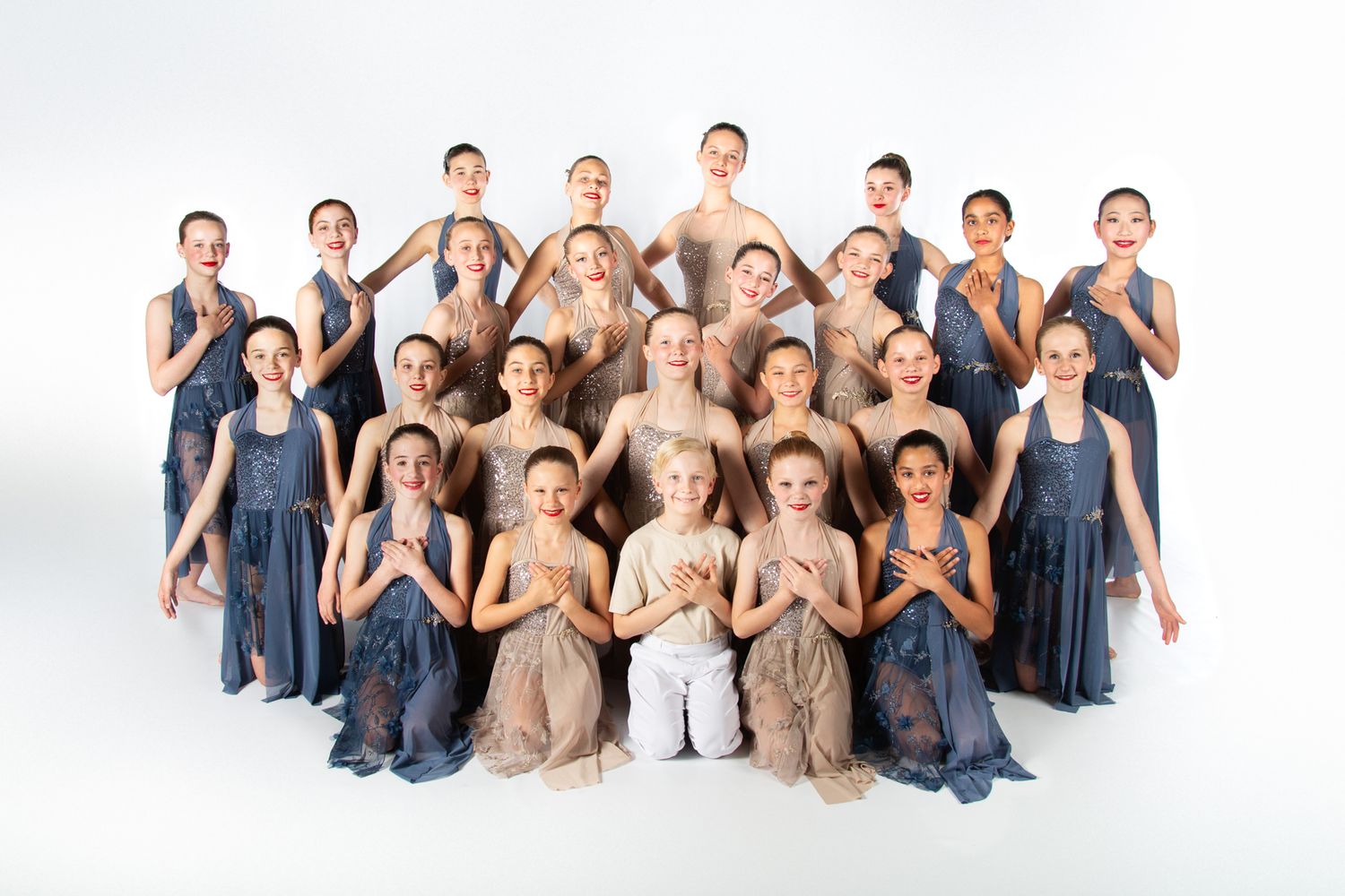 Dance group poses in coordinated blue and tan dresses in studio formation.